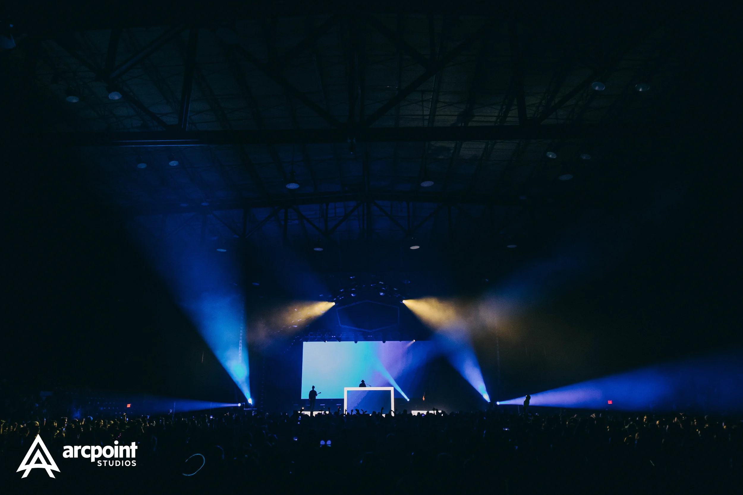 Concert stage with colorful lights, large screen, and an audience in a dark indoor venue, branding 'arcpoint STUDIOS' in the bottom left corner.