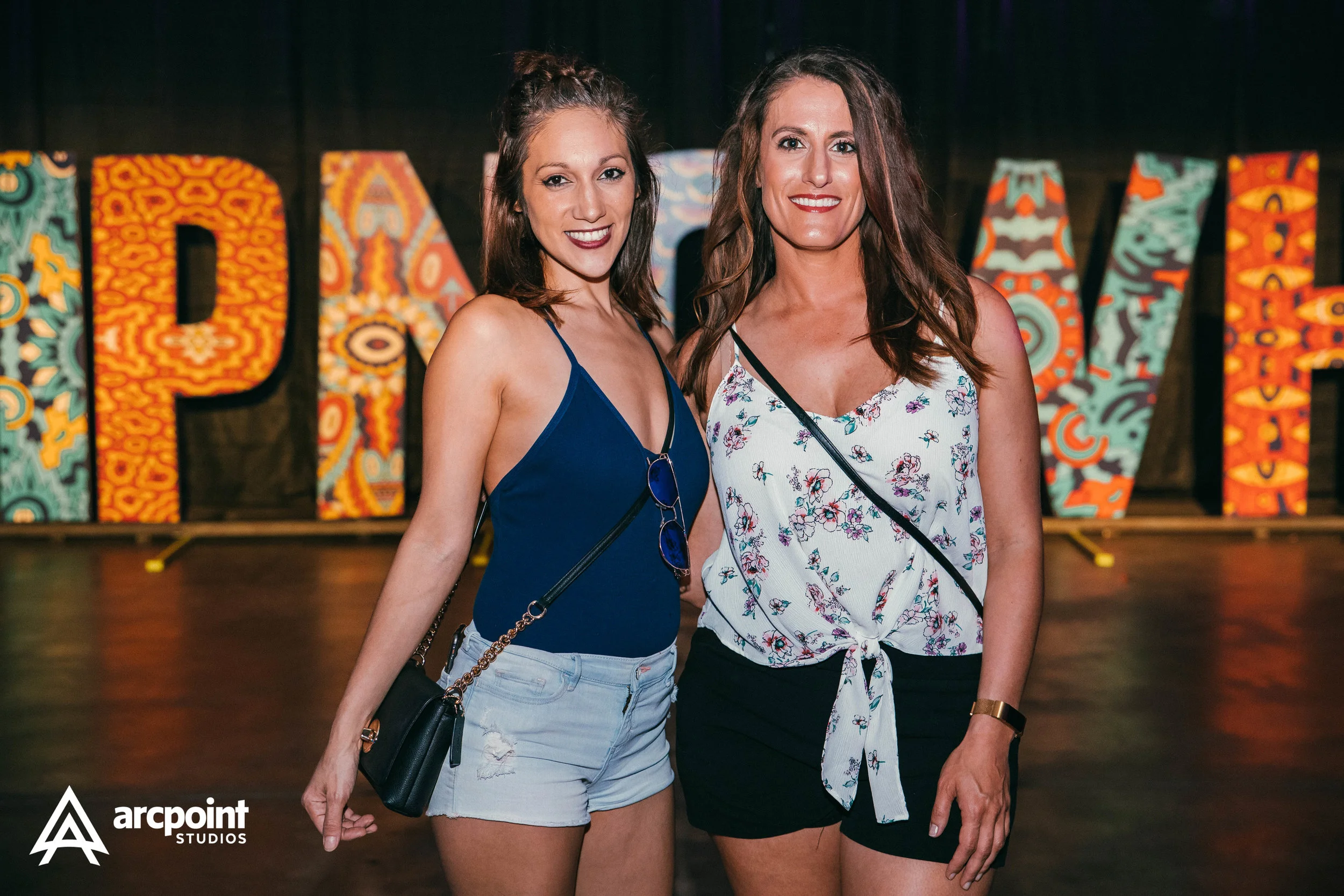 Two women standing together at an event with colorful large block letters behind them that spell 'PARTY'