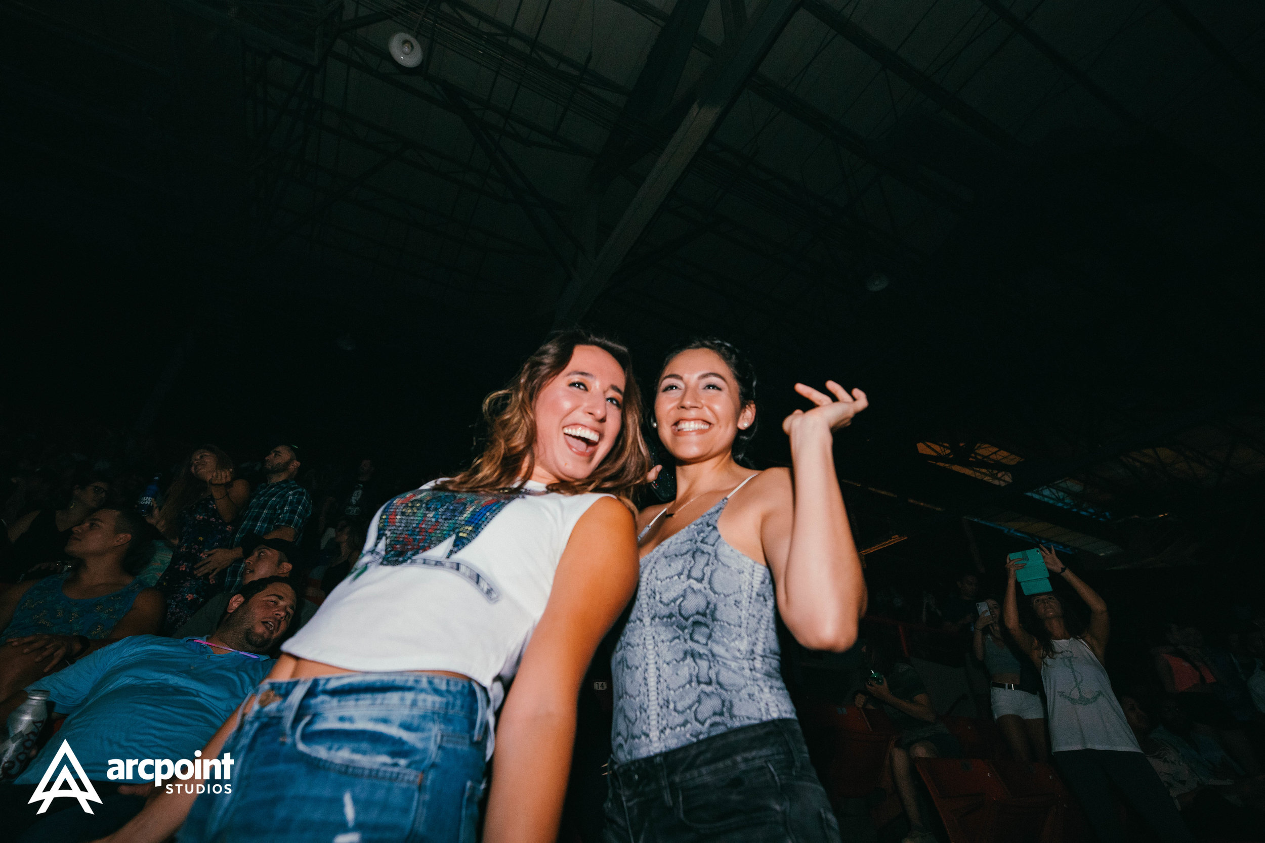 Two women smiling and posing for a photo at a concert or event with a crowd in the background.