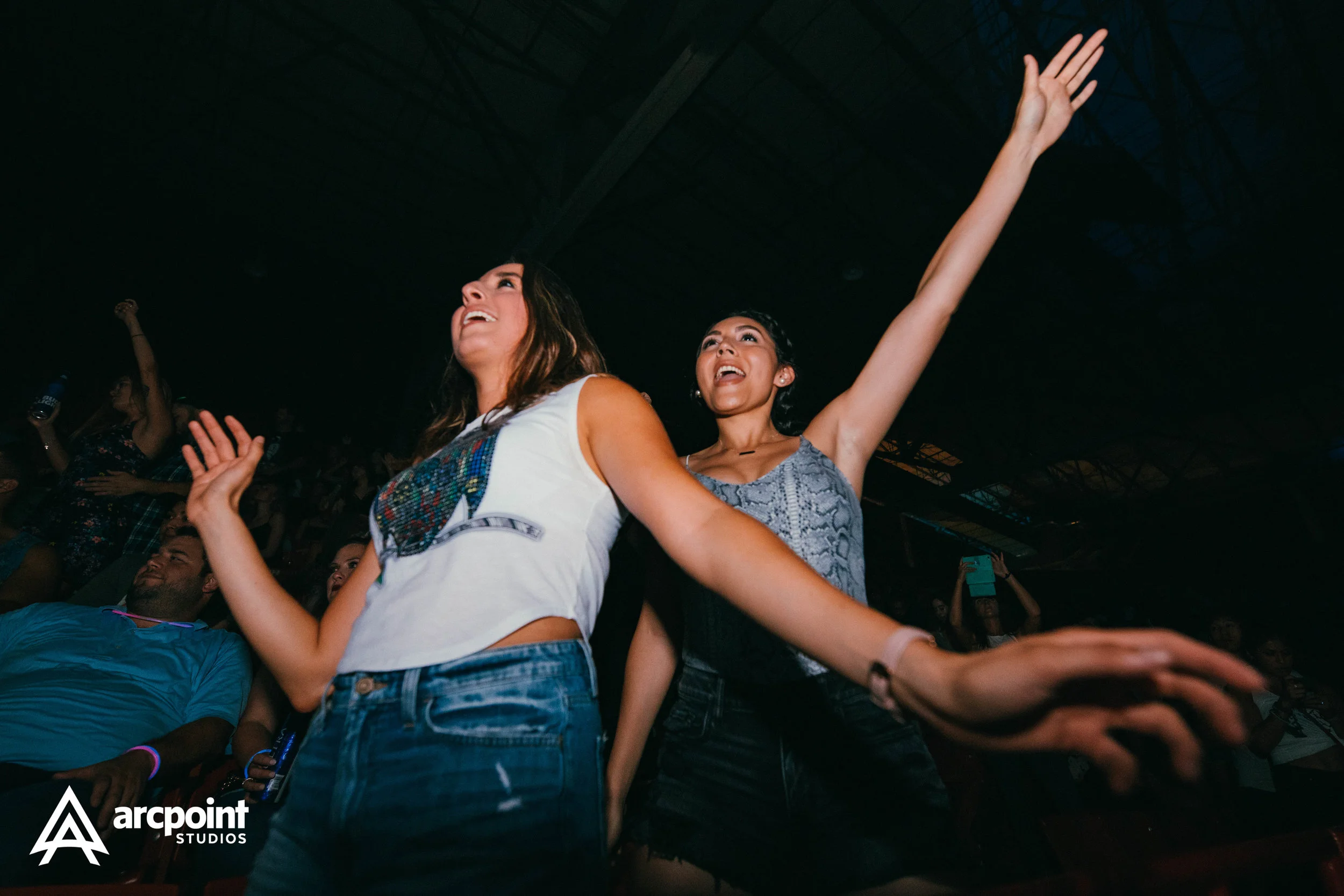 Two women dancing and enjoying themselves at a concert or event, with their arms raised and smiling.