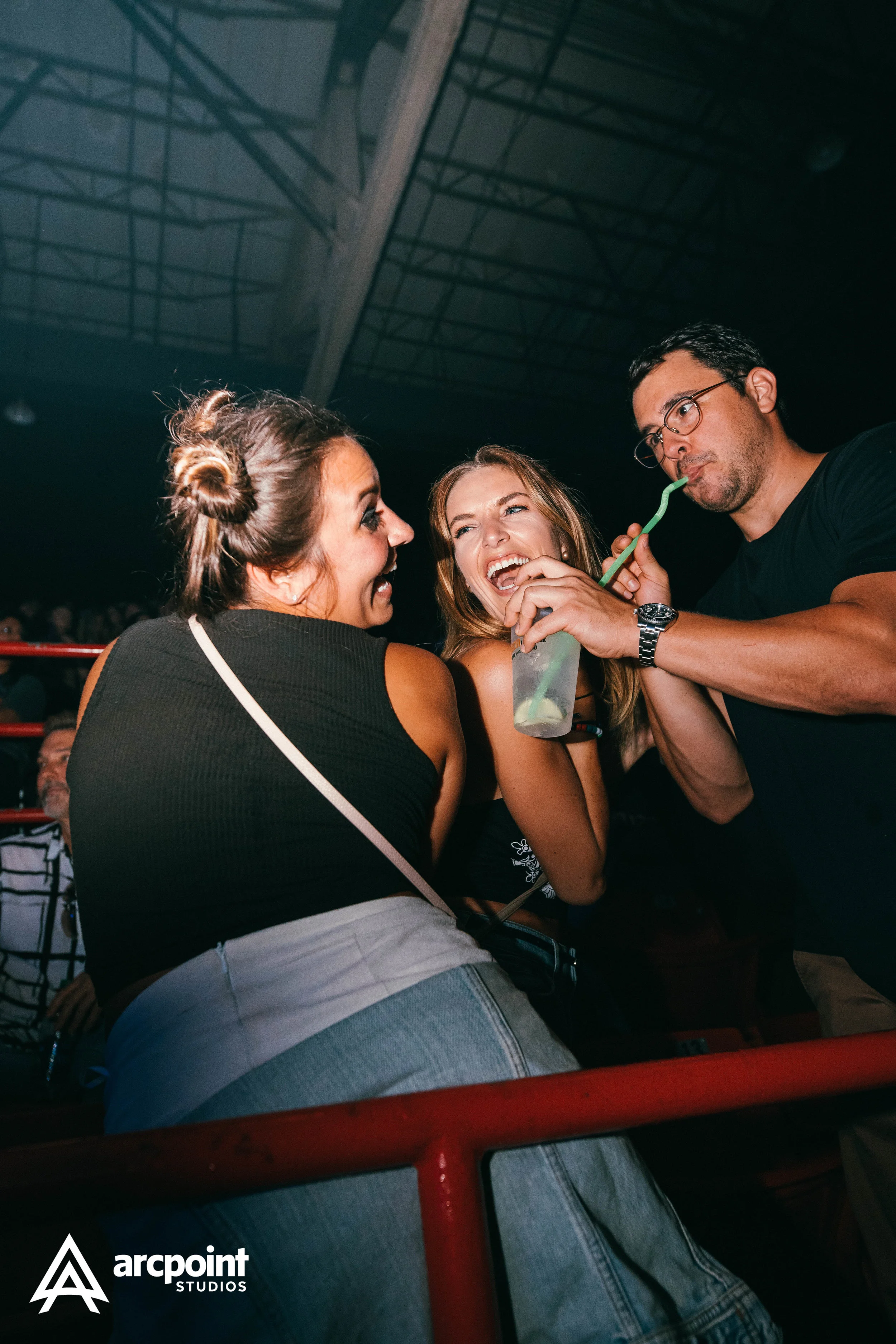 Three friends enjoying drinks and having fun at a crowded indoor event.