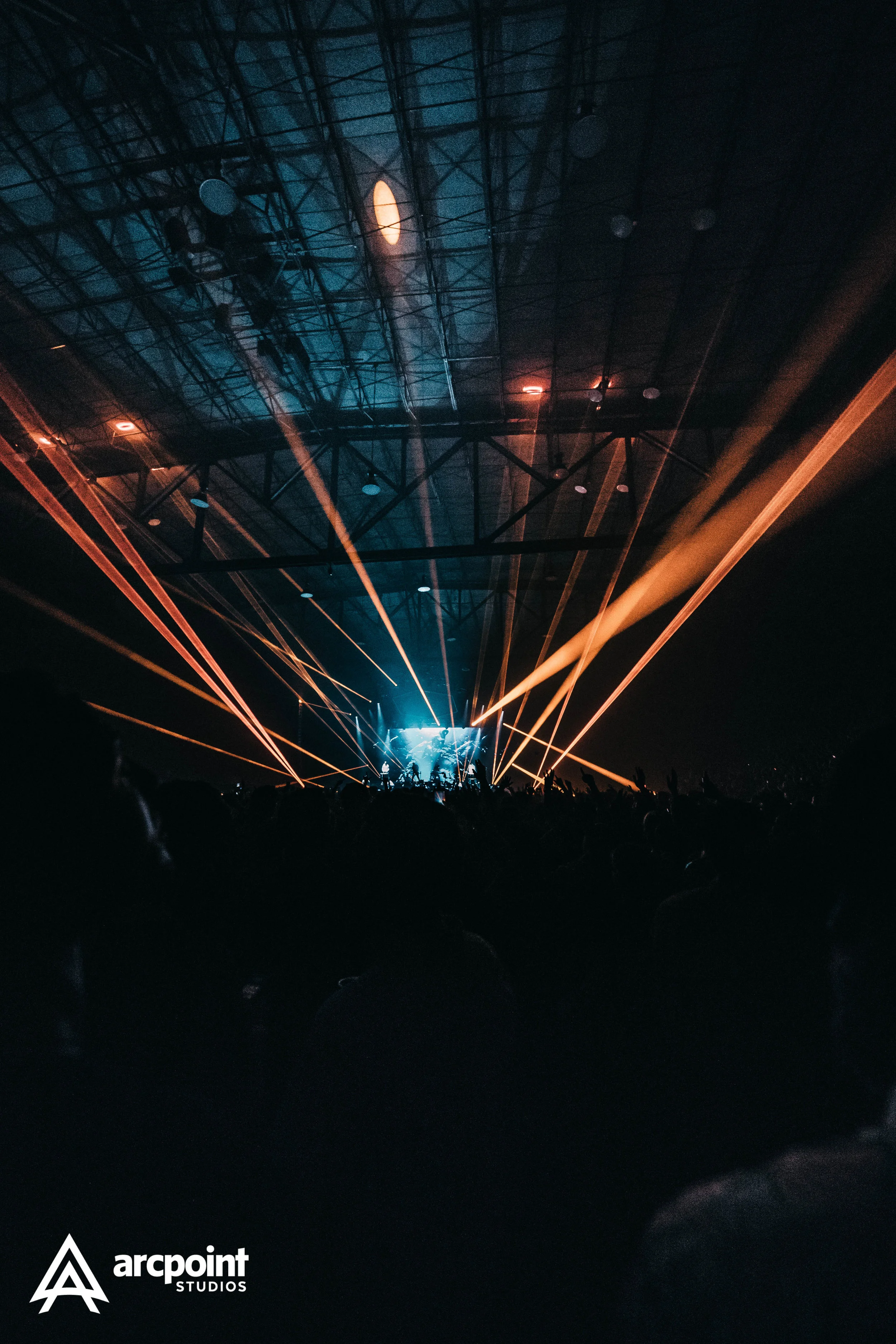 Concert venue with stage, bright blue lighting, and multiple orange laser lights beams extending from stage to ceiling.