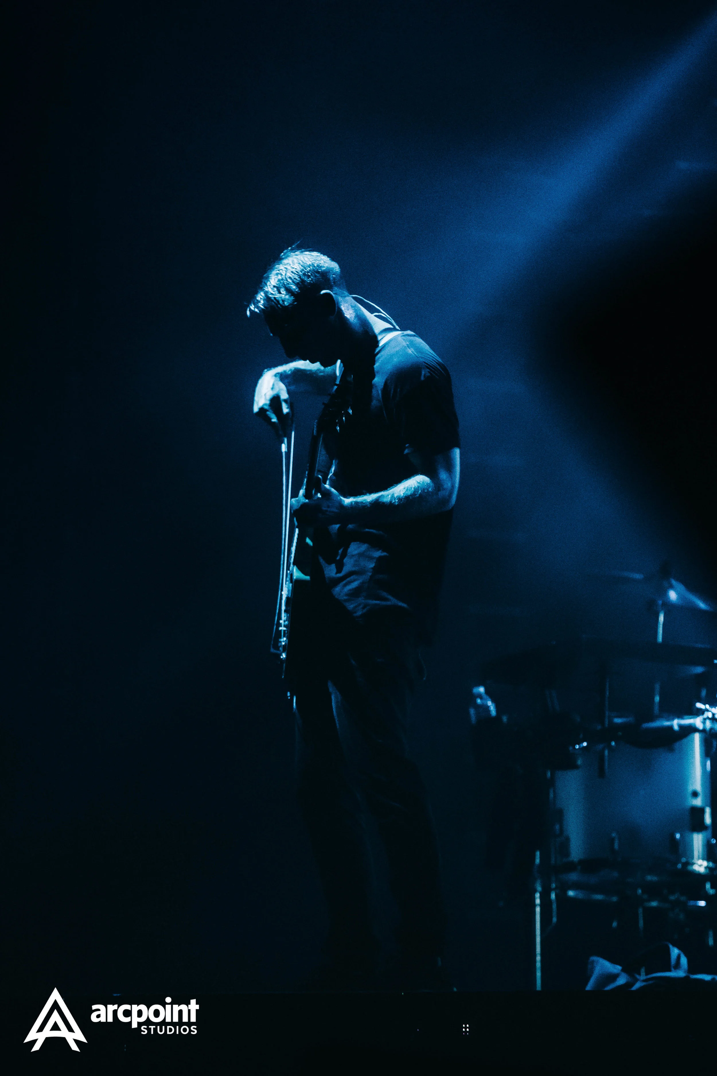 A musician playing a guitar on stage with blue lighting, with a dark background and the logo 'arcpoint STUDIOS' in the bottom left corner.