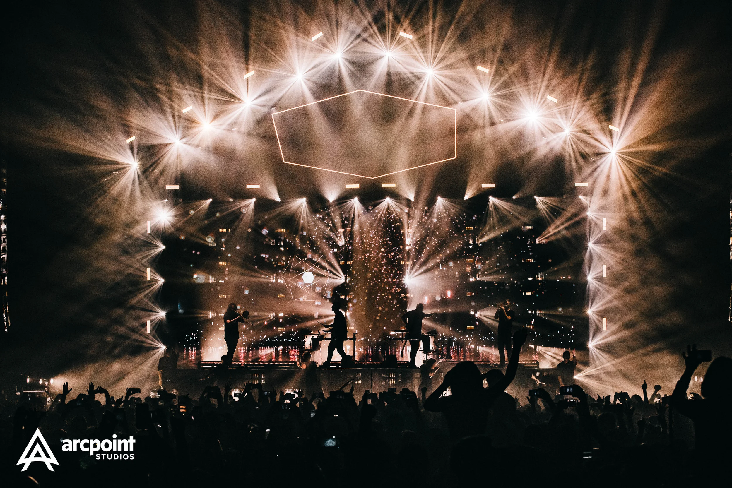 Concert stage with performers and bright, elaborate light show, silhouettes of audience members with some raising hands, and a logo for Arcpoint Studios in the corner.