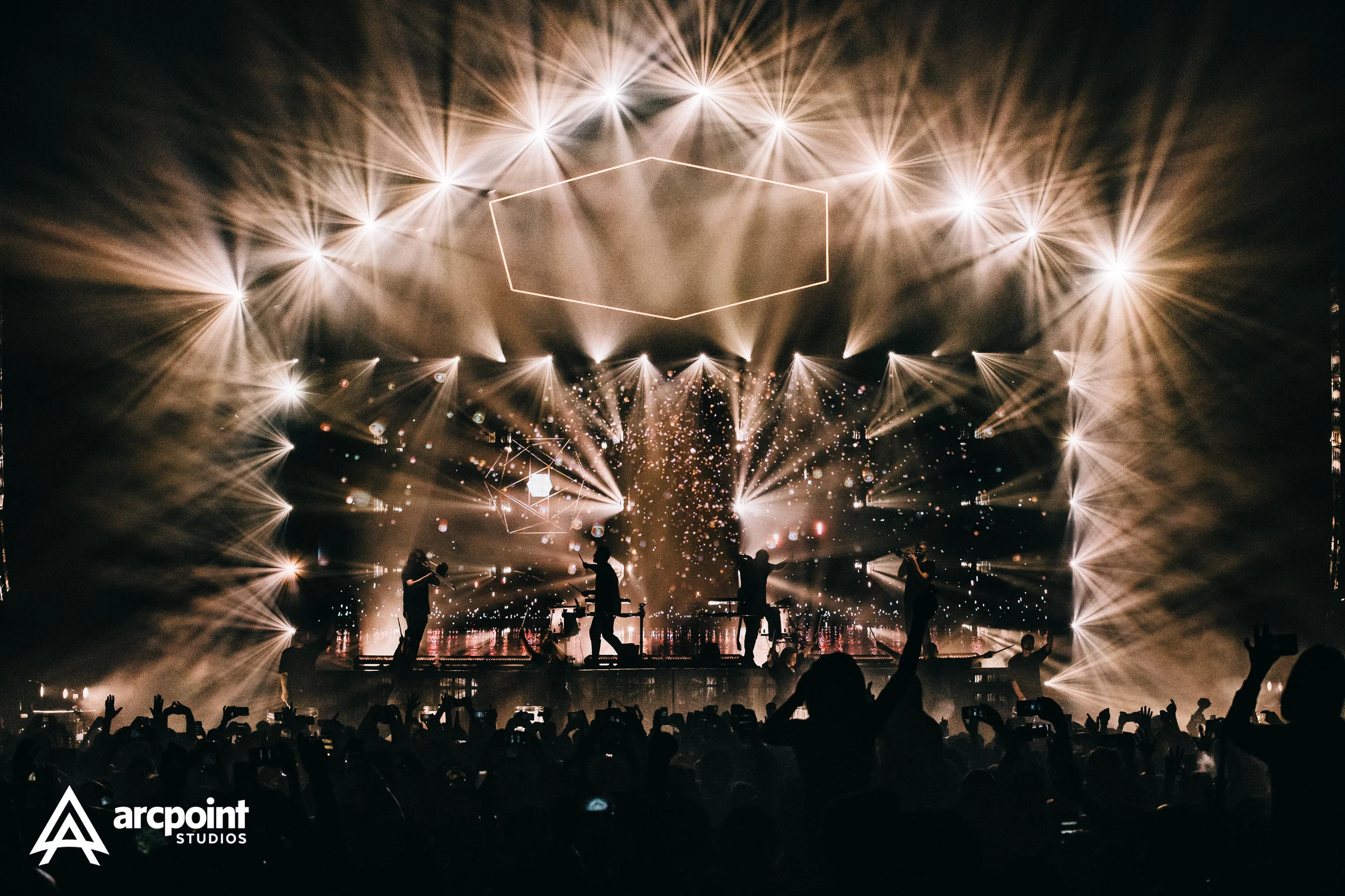 A concert stage with performers, bright lights, and special effects, with an audience in the foreground.