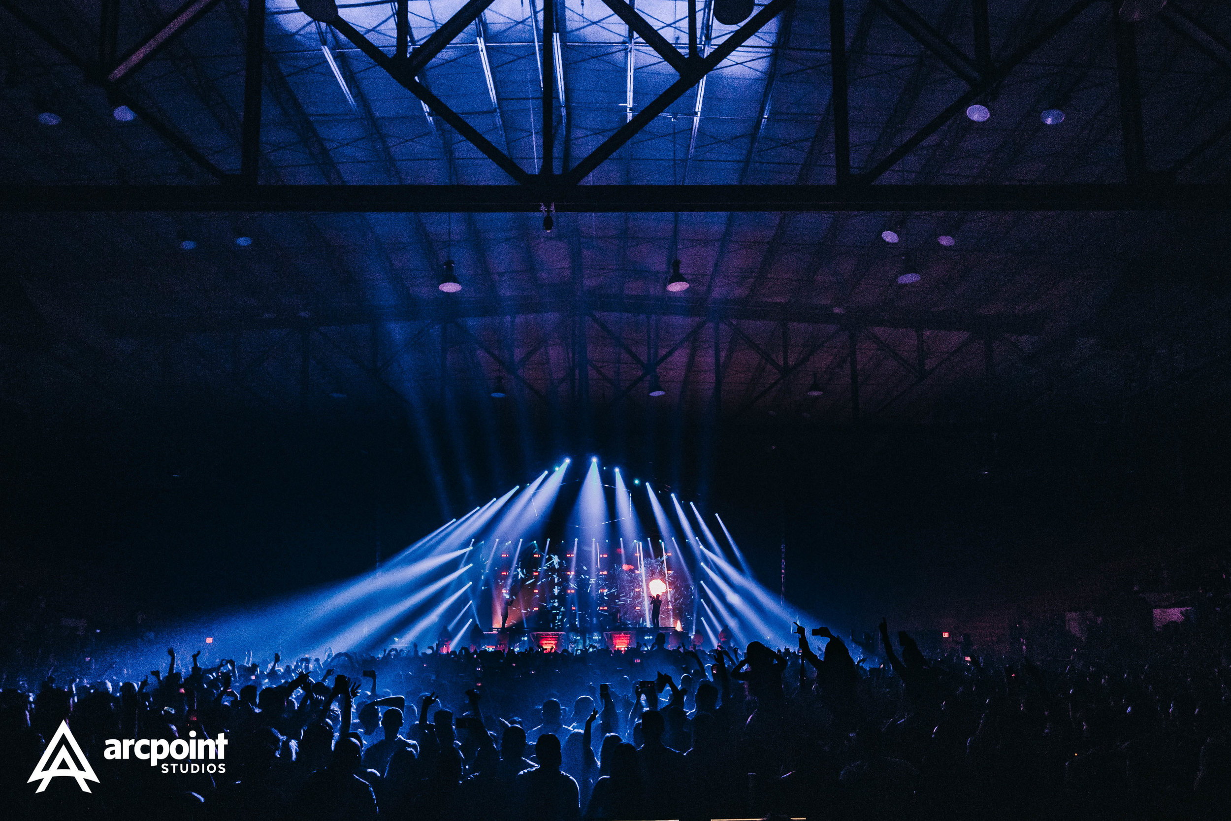 Crowd at a concert with blue and white stage lights in a dark indoor arena.