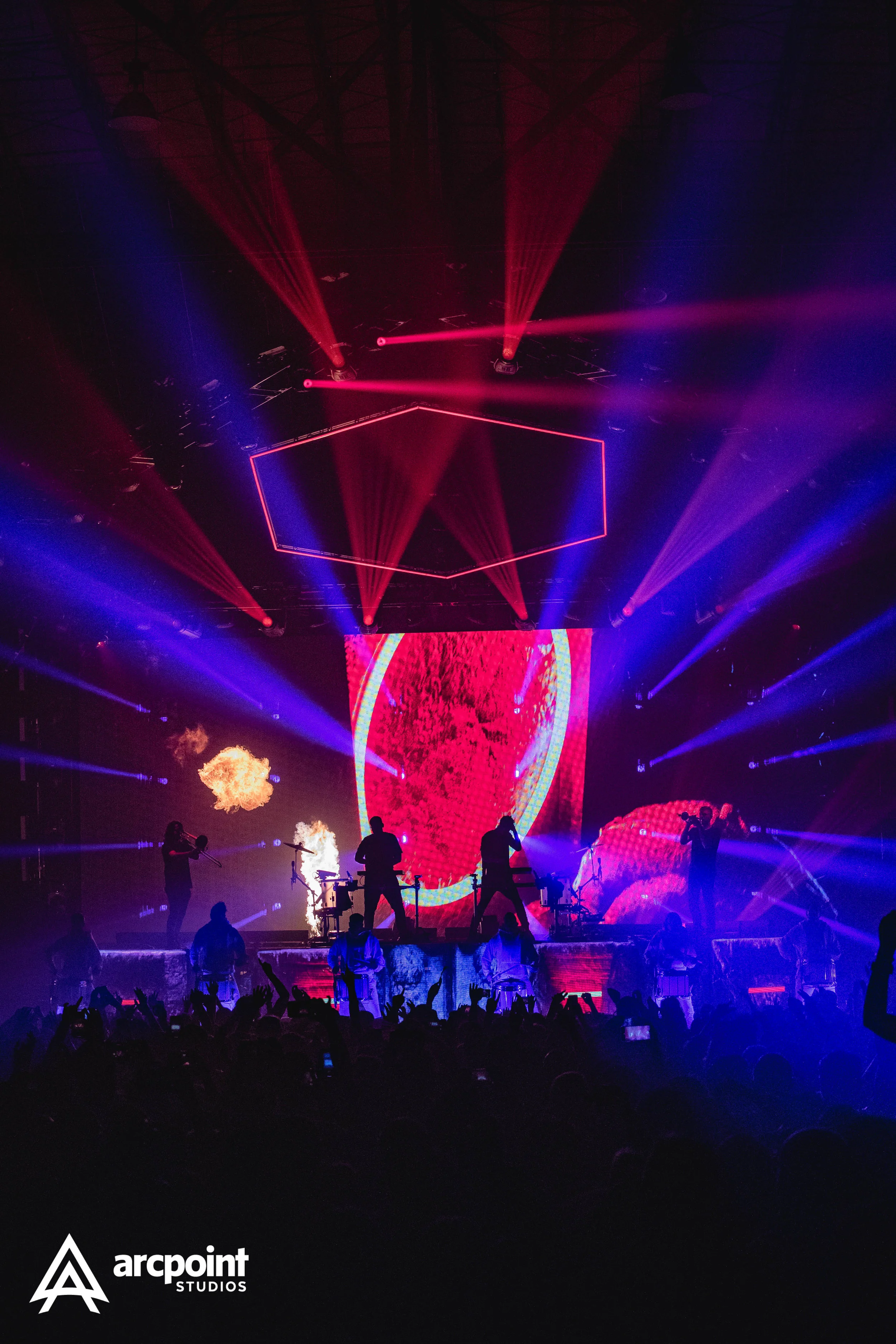 Concert scene with musicians on stage, colorful laser lights, and flames, with the Arcpoin Studios logo in the bottom left corner.