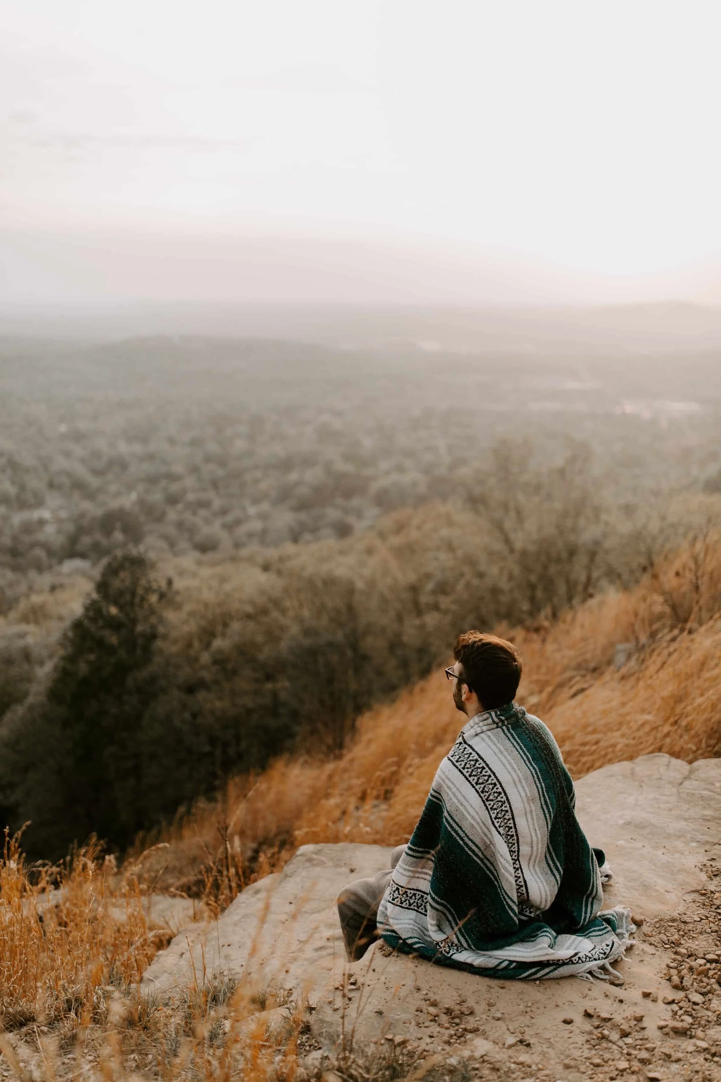 Man sitting on a rock looking out at a forested canyon