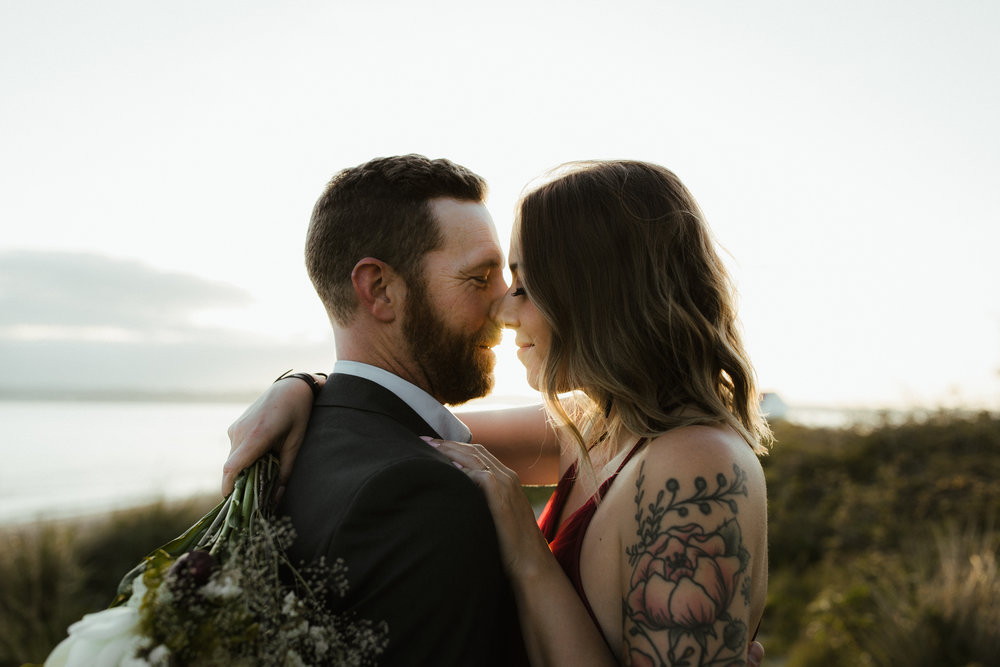 An engaged couple embrace on the beach at discovery park in seattle during sunset