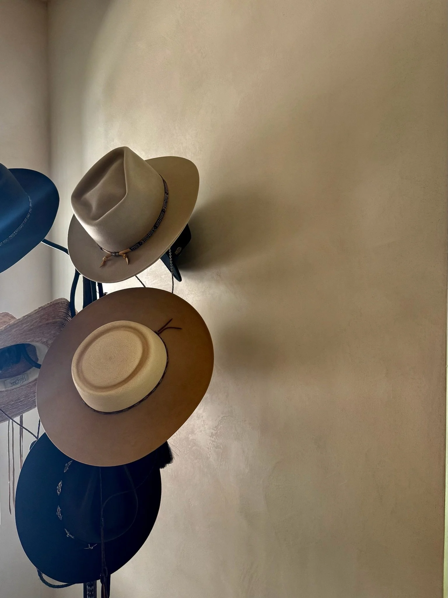 Softly textured Loma natural plaster wall with hats casually hanging from hat rack.