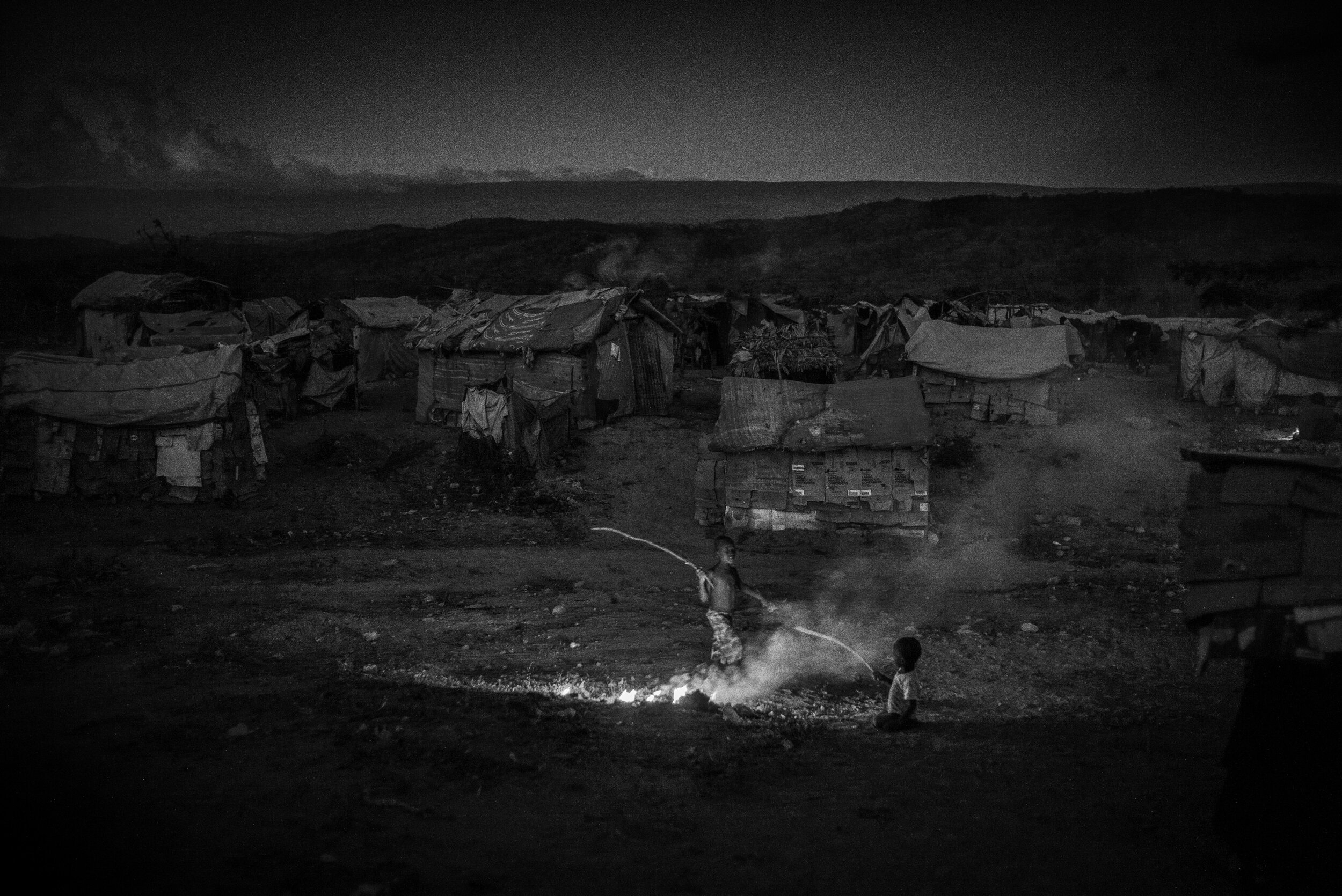  Photo of boy standing by a fire at night, lit by the flames 