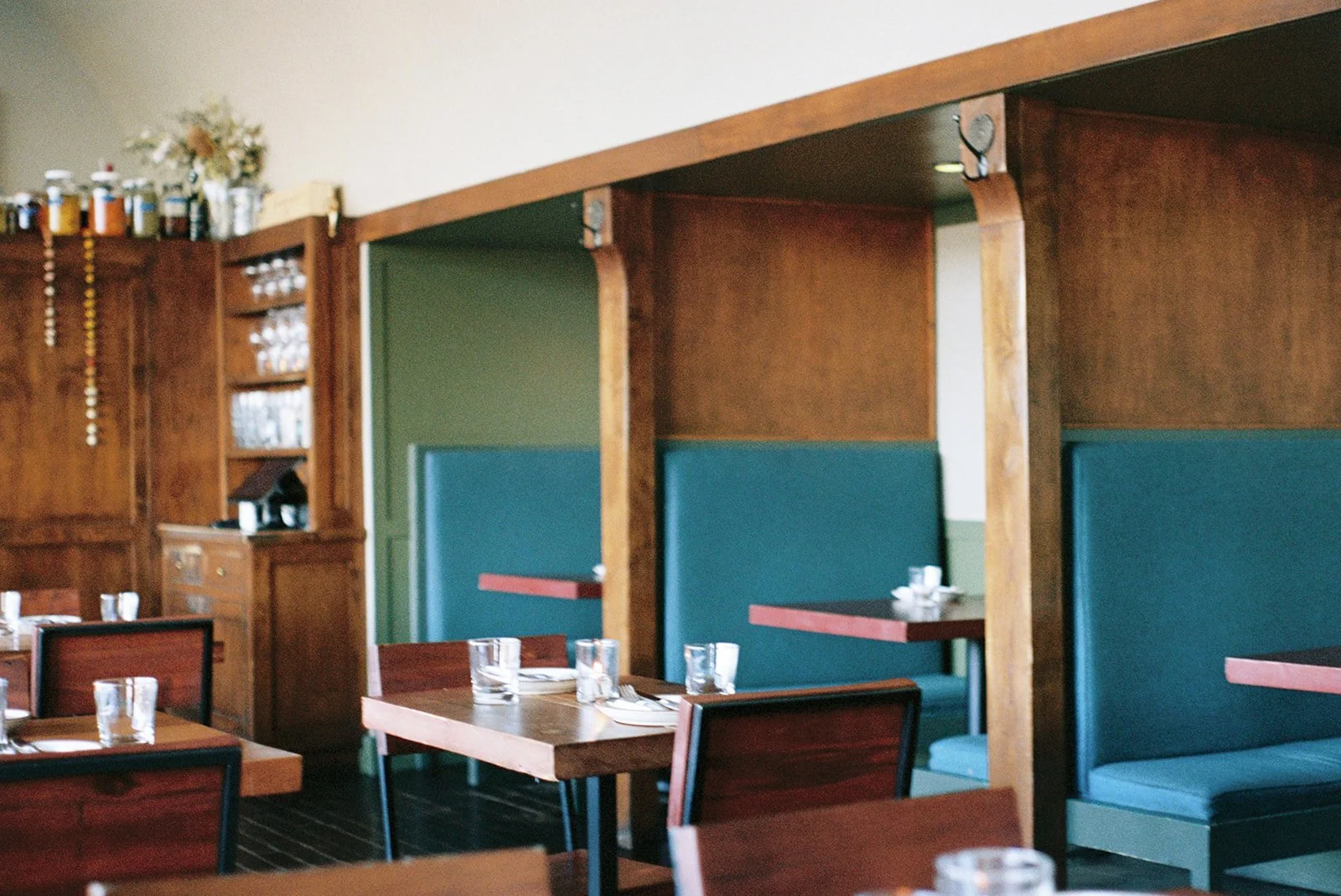 Interior of a restaurant with wooden booths, teal seats, and tables set with glasses and silverware.