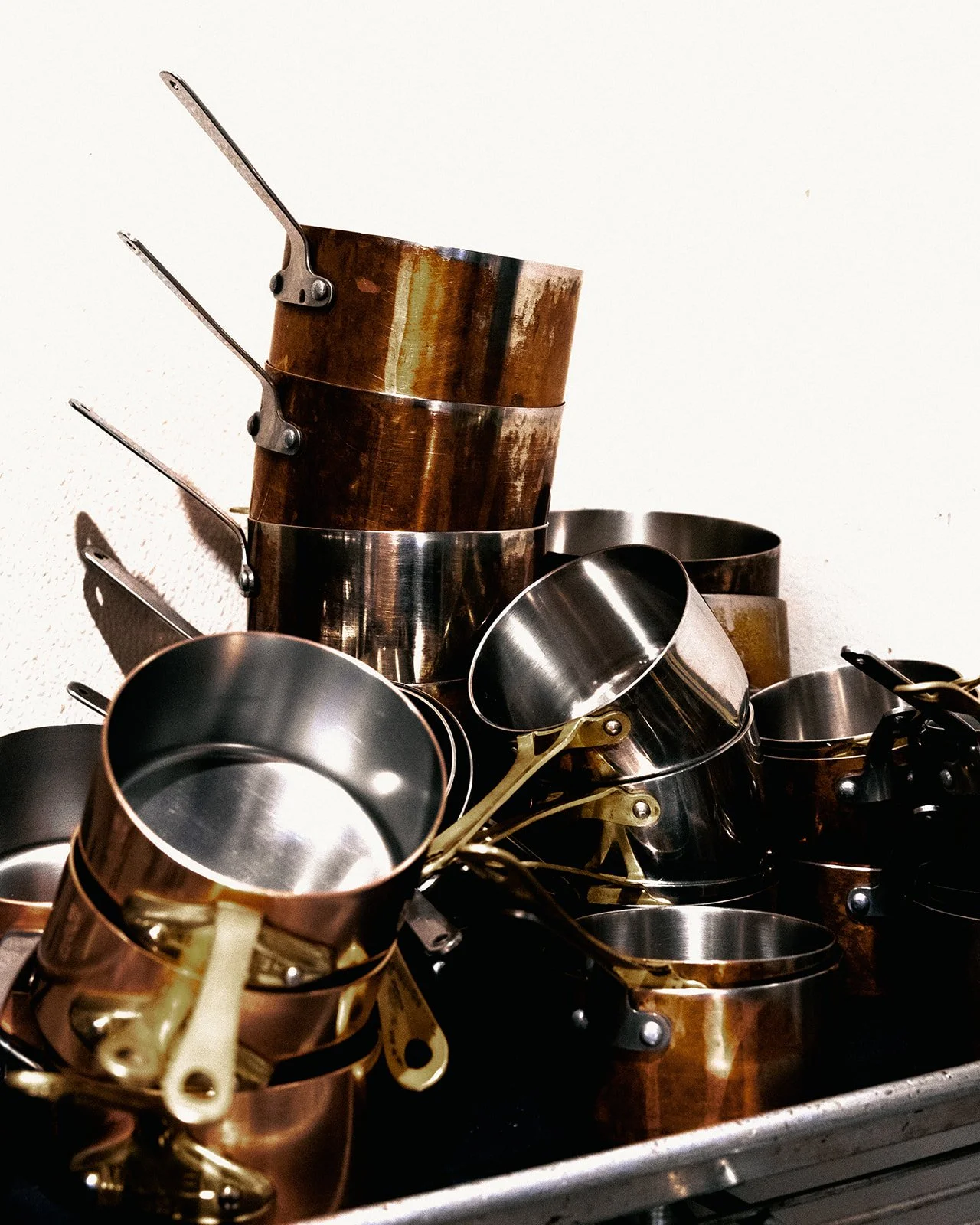 An assortment of stacked metal measuring cups and baking molds, some with a copper finish, placed on a countertop.