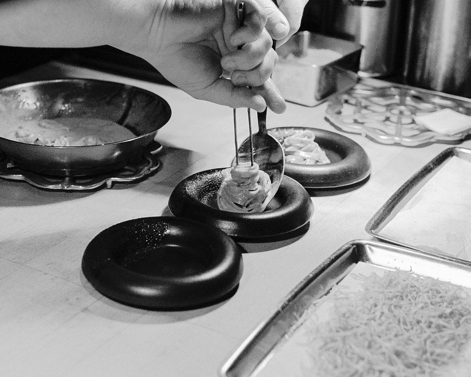 hands twirling pasta with tongs and a spoon into a small, black bowl