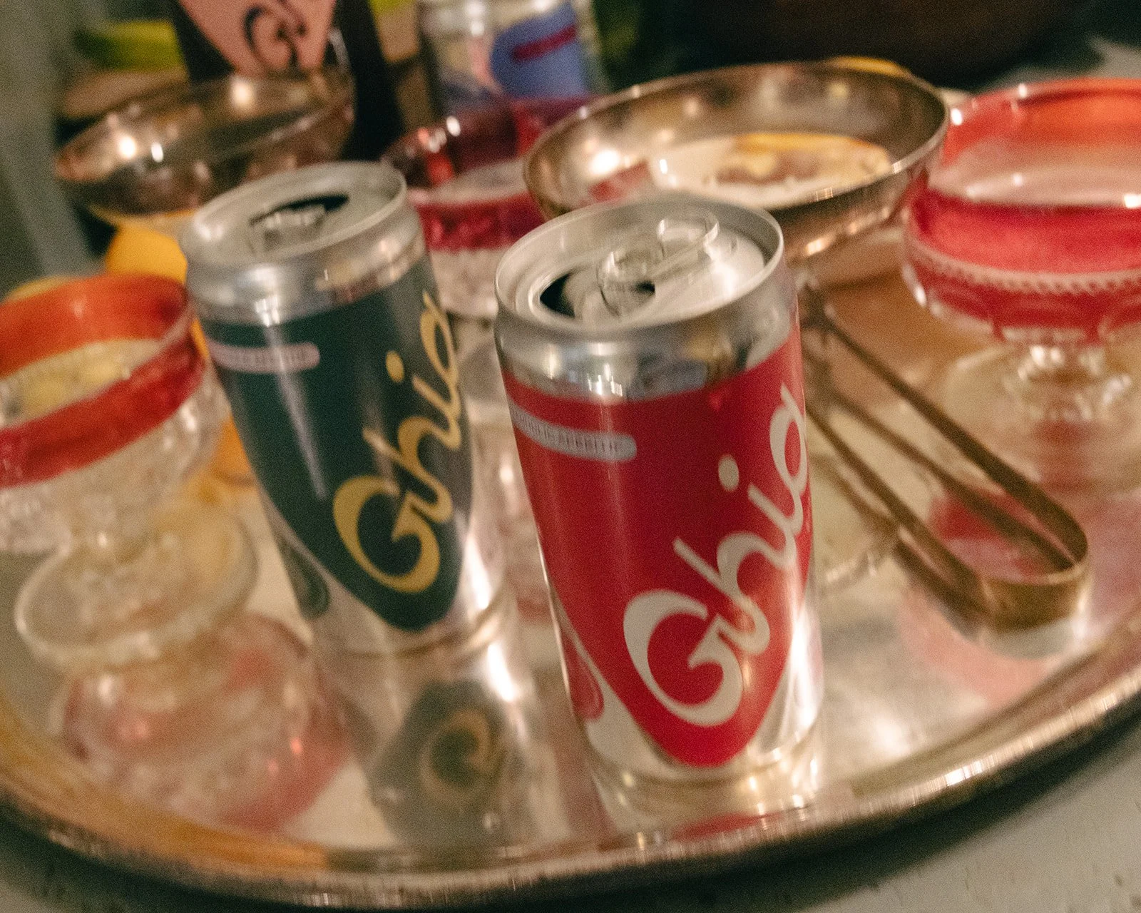 Coca-Cola soda cans on a silver tray surrounded by small glasses with colorful drink rims.
