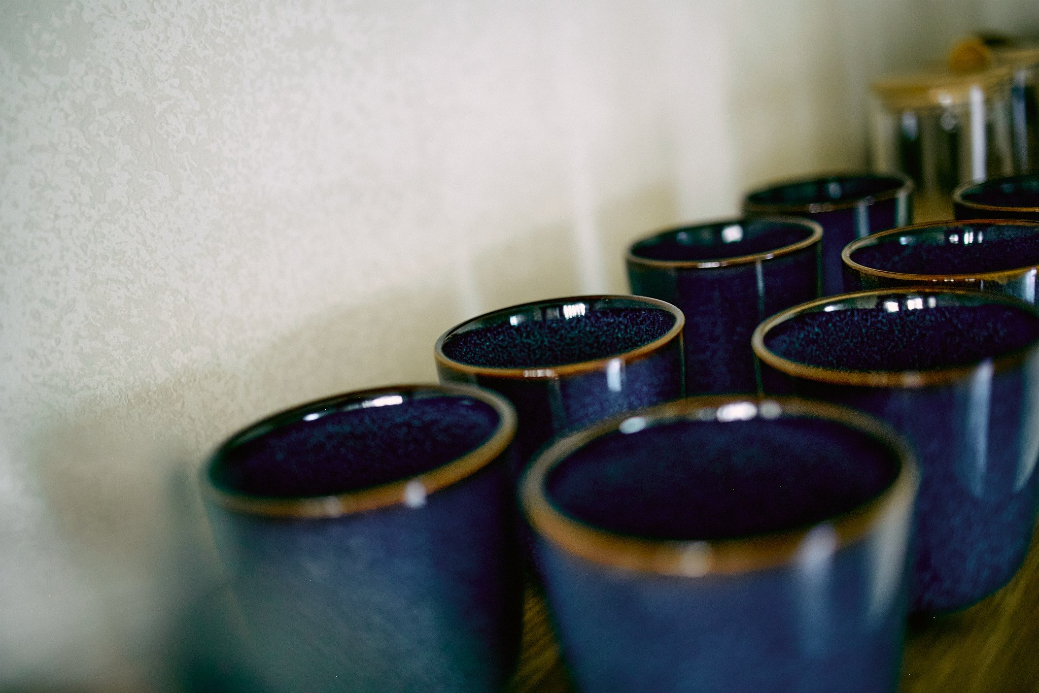 Close-up of several black cups with gold rims, arranged in rows, against a plain light-colored wall.
