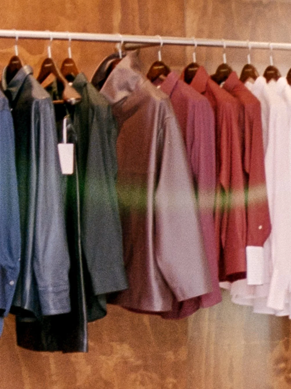 A row of men's dress shirts in various colors hanging on a rack.