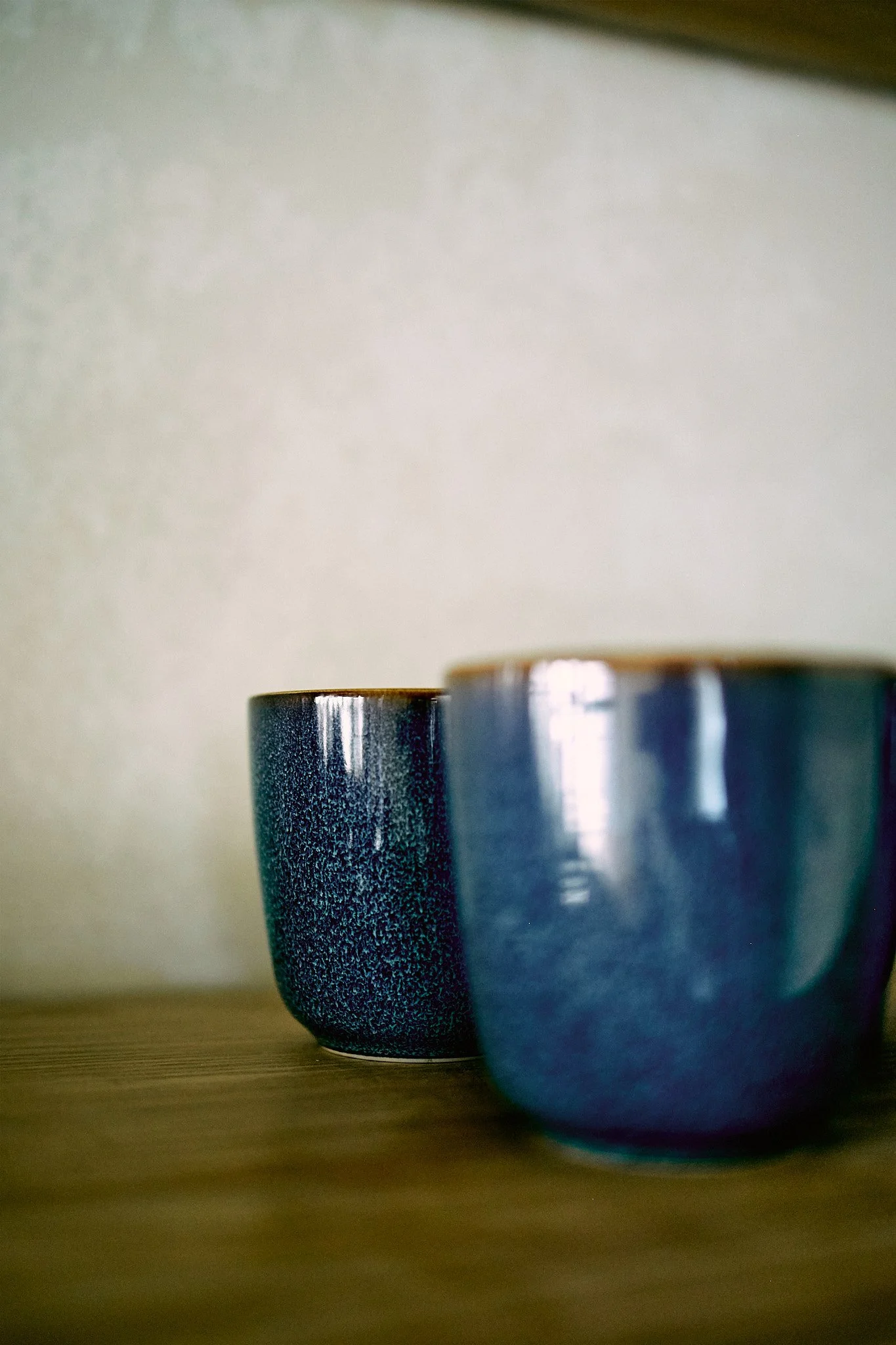 Close-up of two ceramic cups on a wooden surface, background plain wall.
