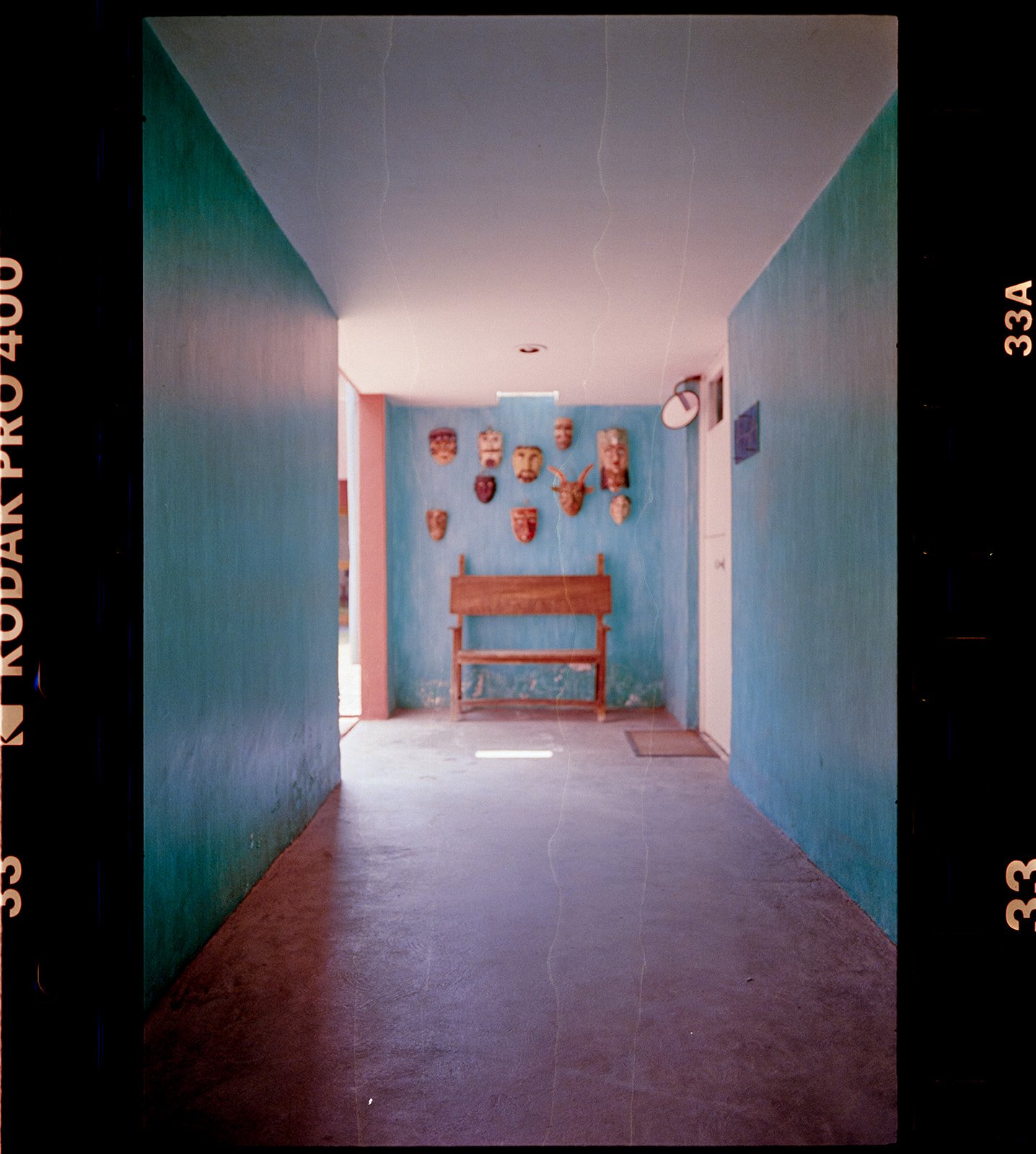 An indoor hallway with teal walls decorated with various tribal masks and a wooden bench at the end.