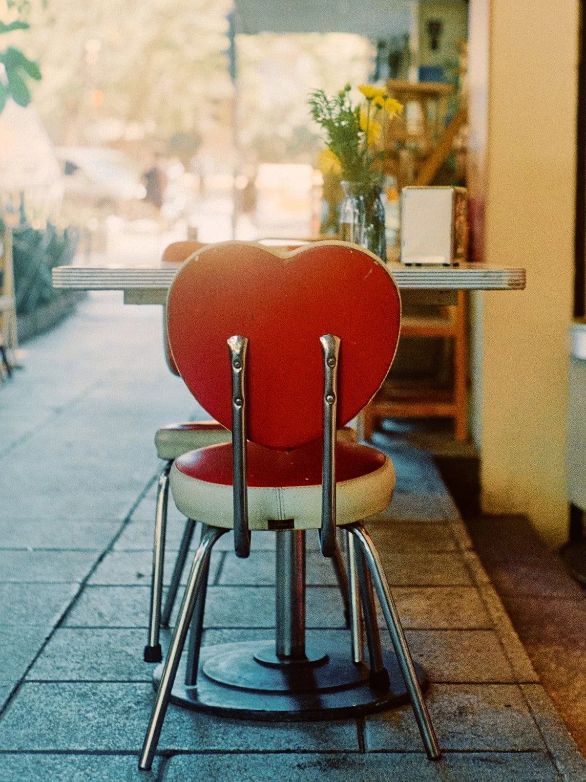 A red vintage chair with a heart-shaped backrest facing a table in a cozy cafe.
