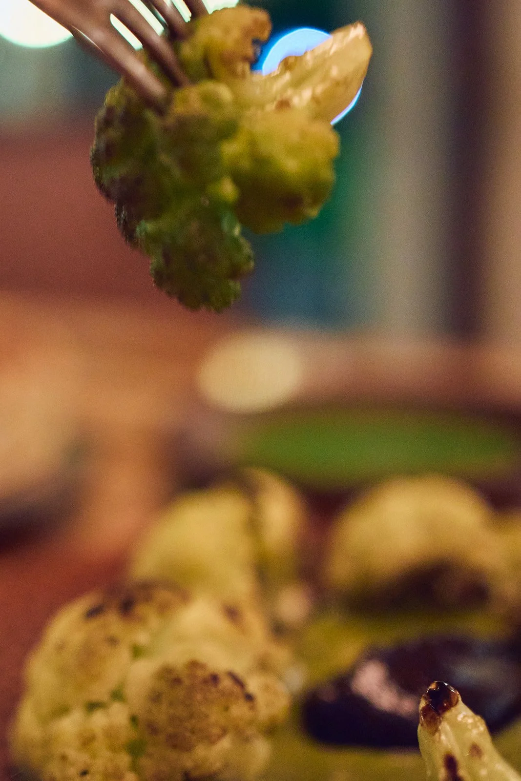 Close-up of a broccoli floret on a fork with blurred background.