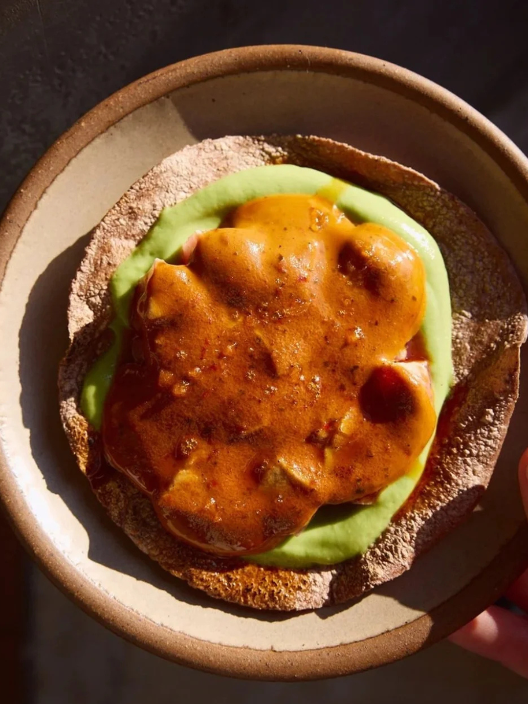 A toasted English muffin topped with mashed avocado and a poached egg covered in a rich, brown gravy.