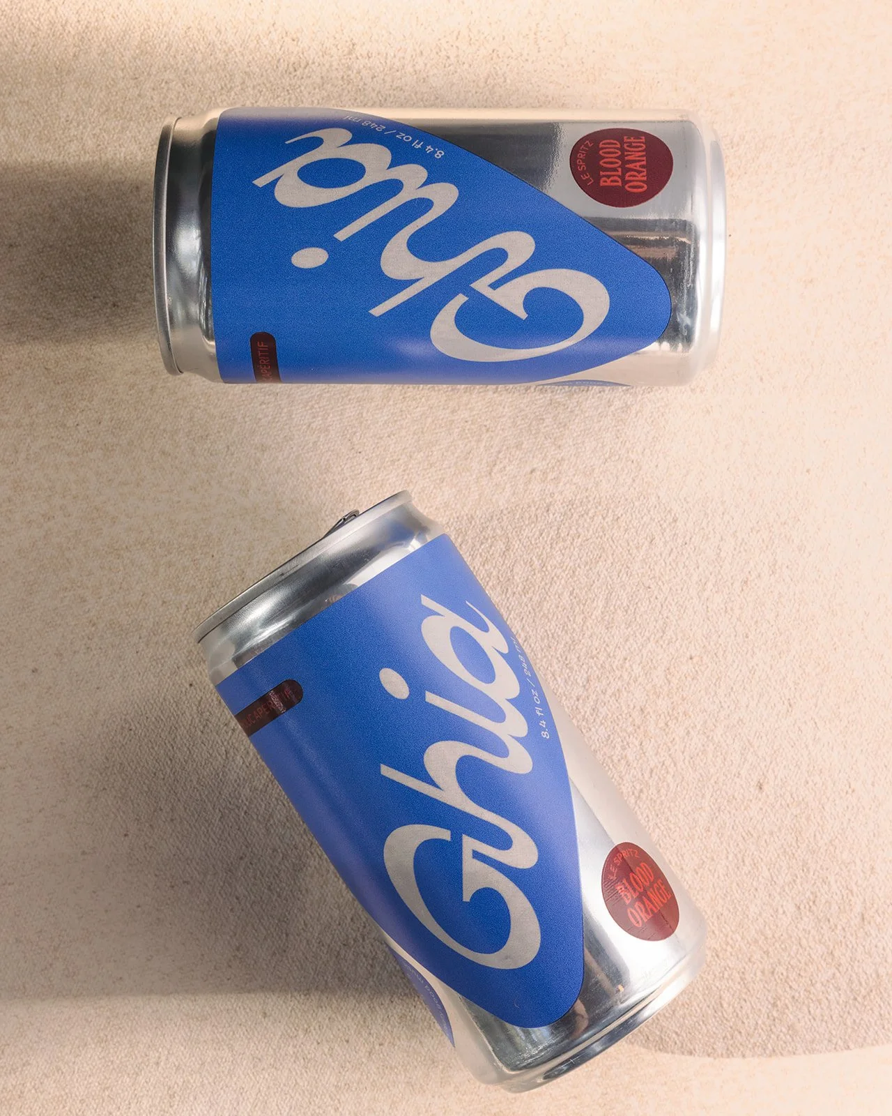 Two cans of Ghia soda, blood orange flavor, placed on a beige surface.