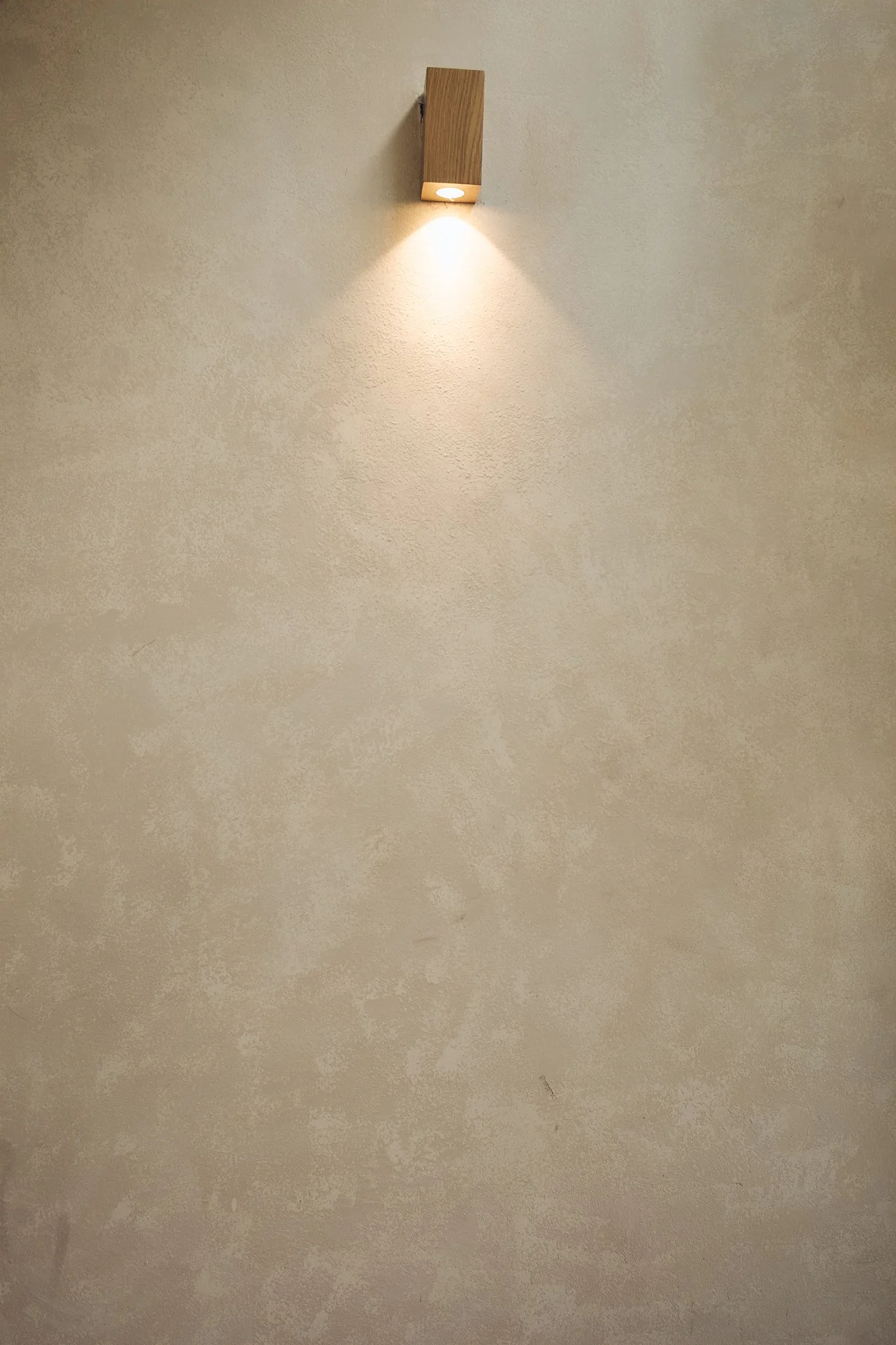 A beige wall with a small, rectangular wooden light fixture attached near the top, casting a downward glow of light.