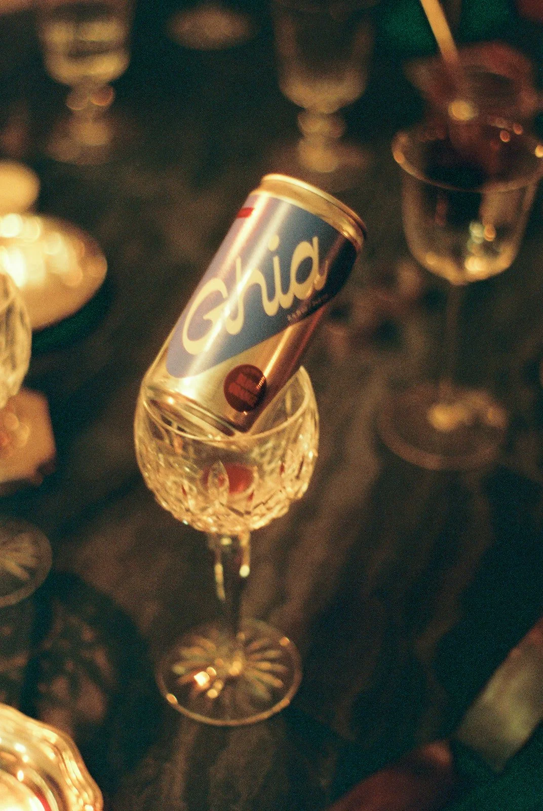 A vintage R确rd soda can is placed inside a decorative glass on a dark table surrounded by various glasses and bottles.