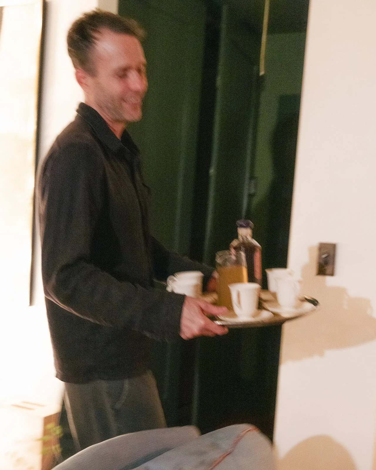 A man in a black jacket holding a tray with coffee cups, syrup bottles, and a jug.
