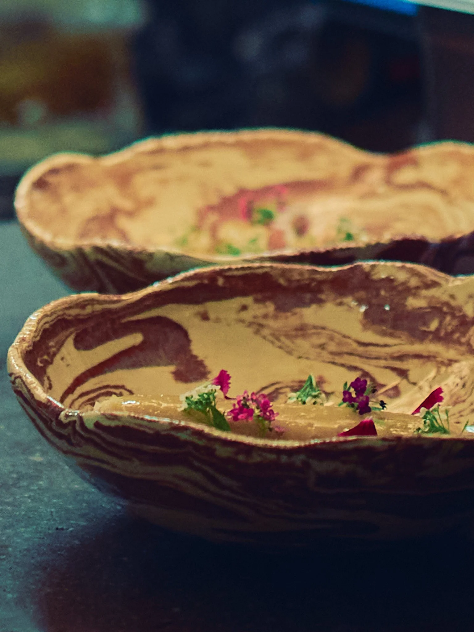 A decorative bowl with intricate designs and small colorful flowers inside, placed on a dark surface.