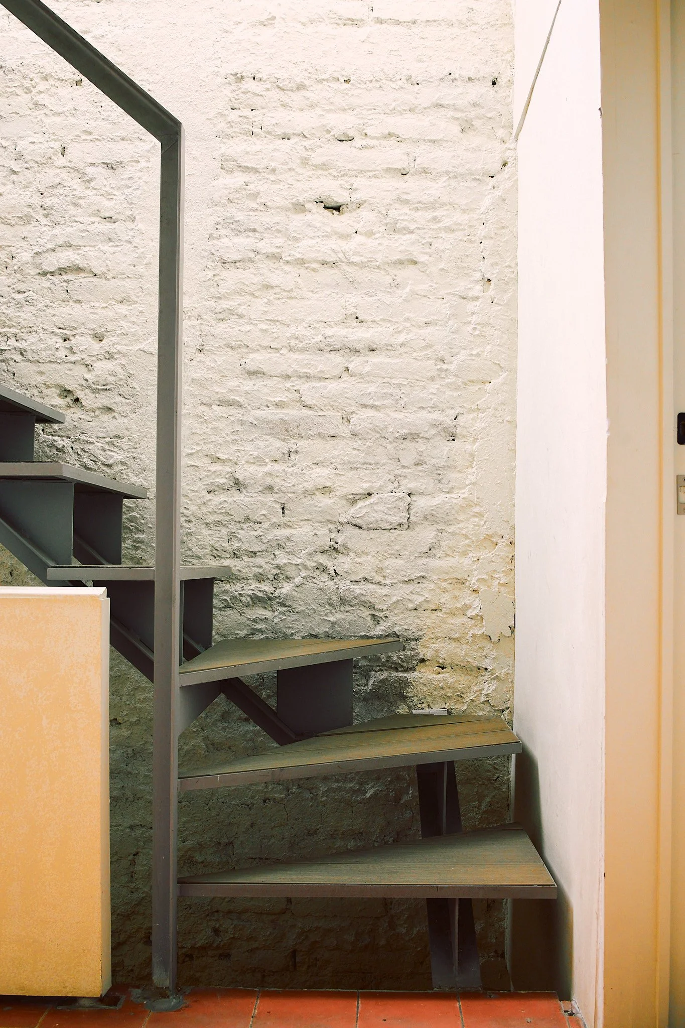 A metal staircase with wooden steps ascending along an unfinished white brick wall.