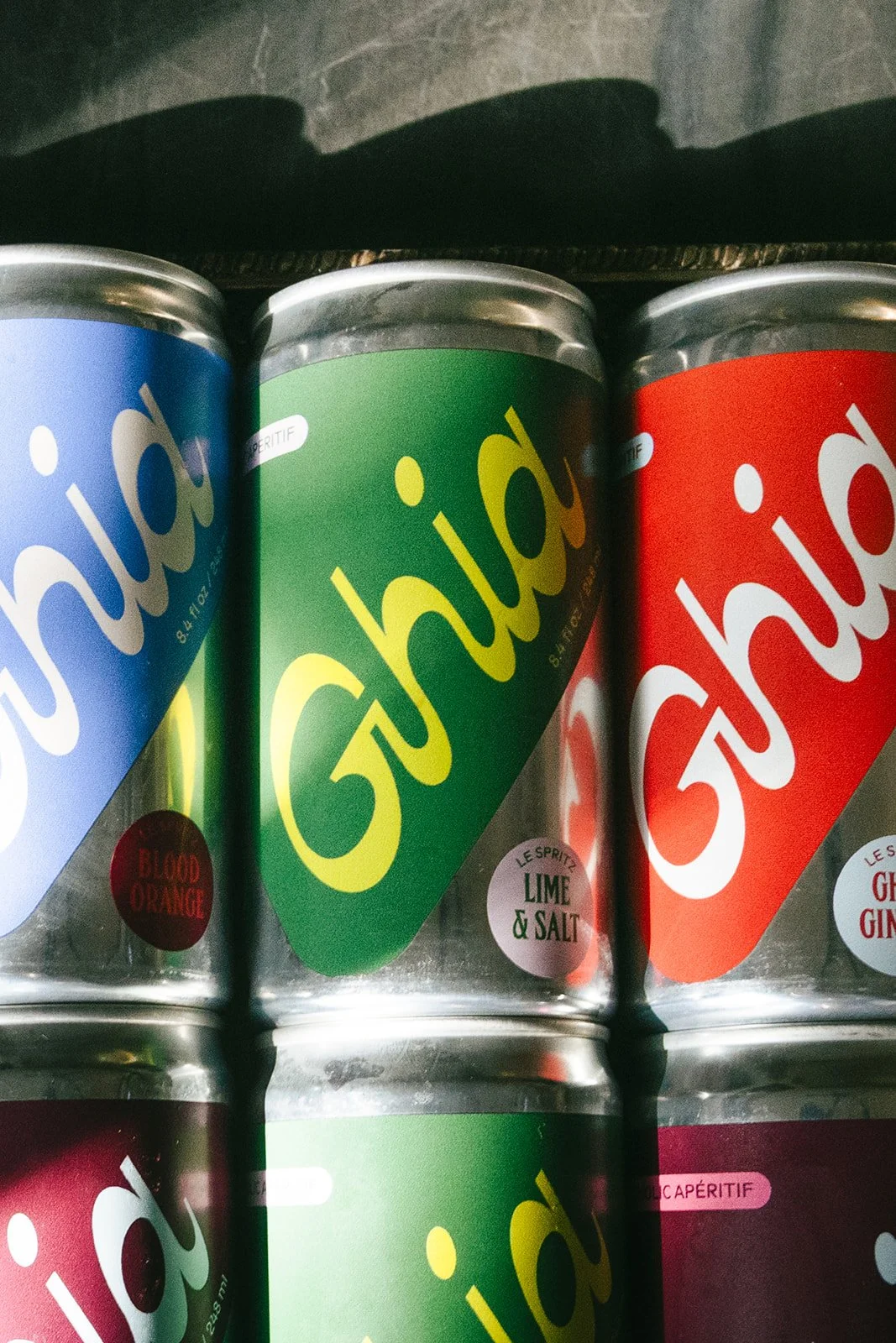 Close-up of colorful cans of Ghia sparkling drink, featuring blue, green, and red labels with the Ghia logo.