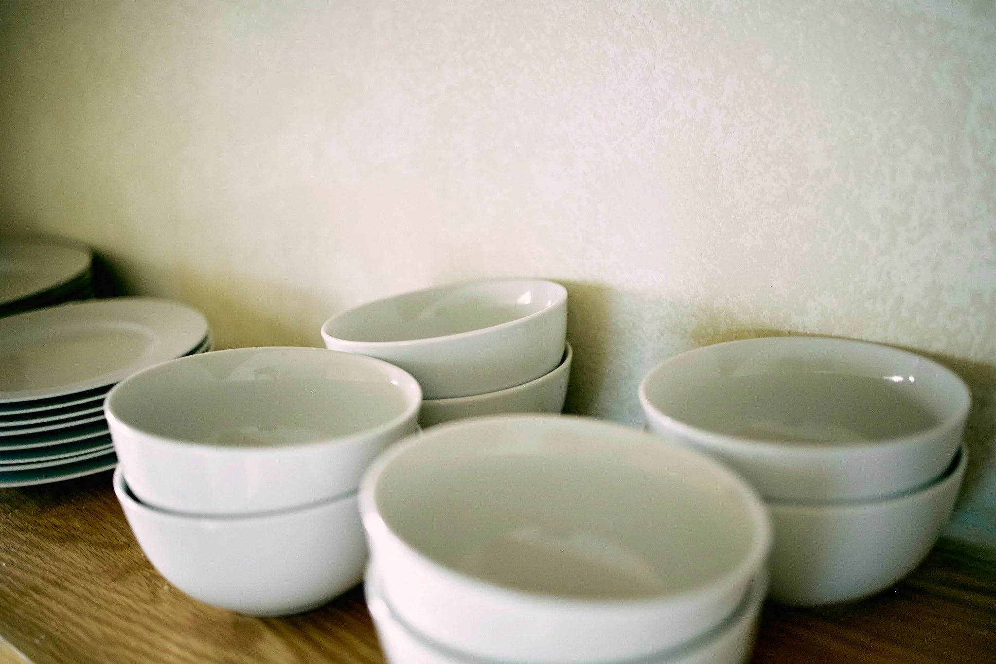 A stack of white ceramic bowls on a wooden surface with a plain background.