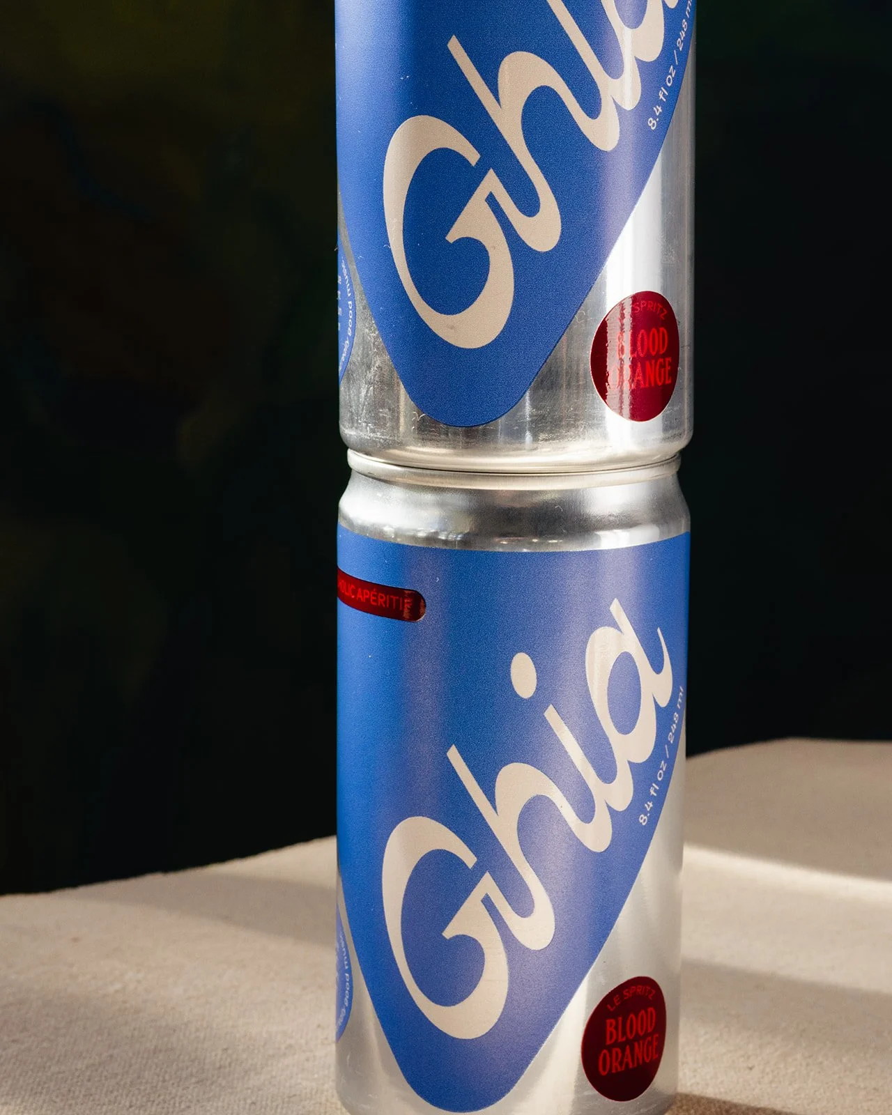 Two cans of Crush Orange soda stacked one on top of the other with black background and some shadowed surface underneath.