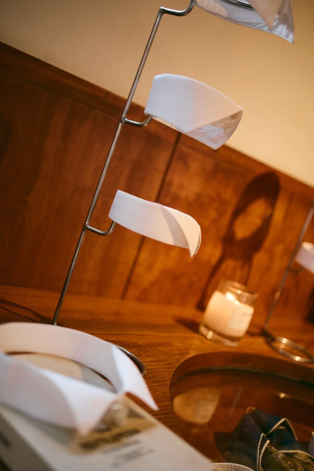 A candle on a wooden table, with a white decorative sculpture, a glass jar of candle, and other objects in the background.