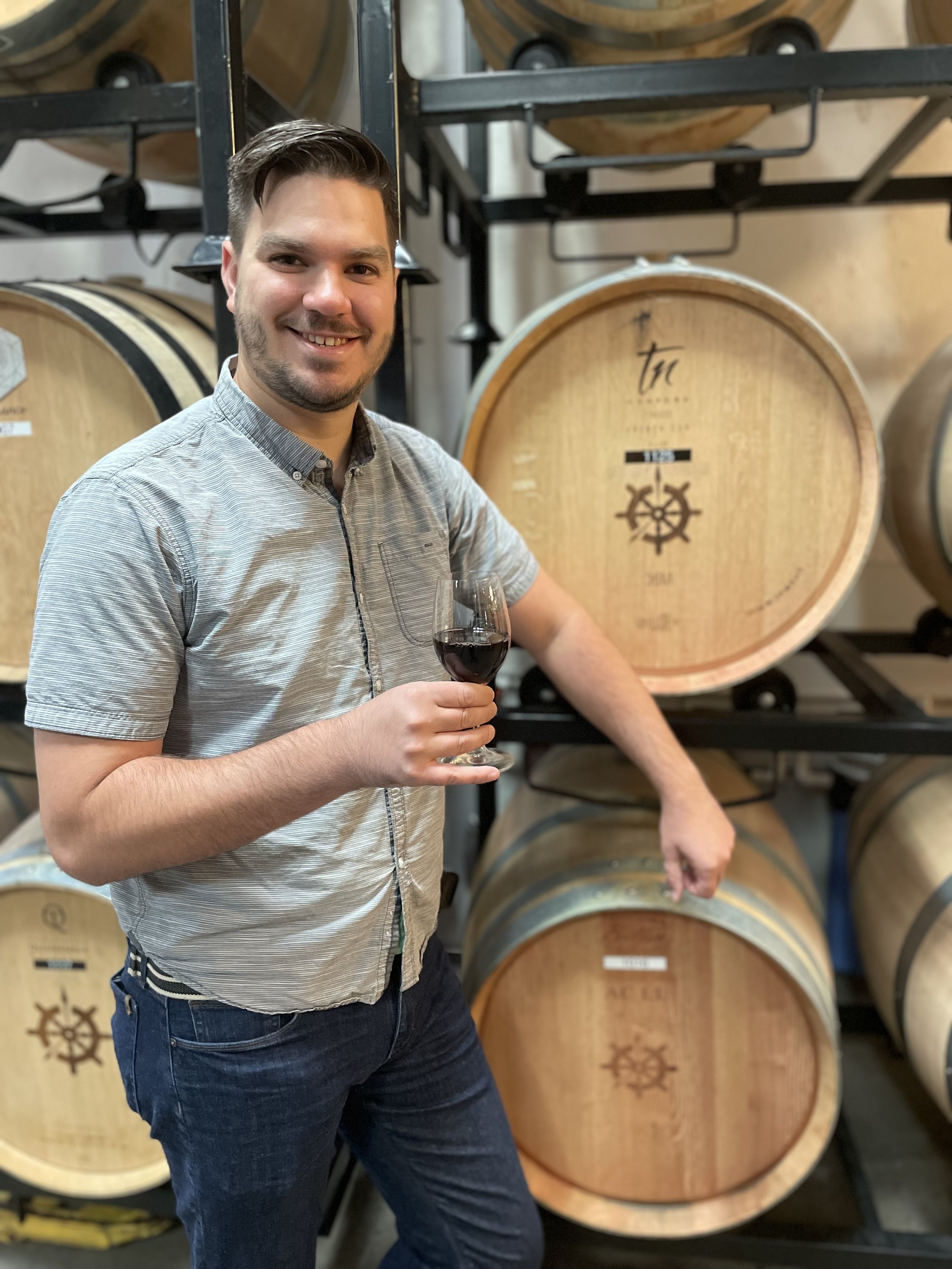 Man standing in front of a wine barrel holding a glass of wine