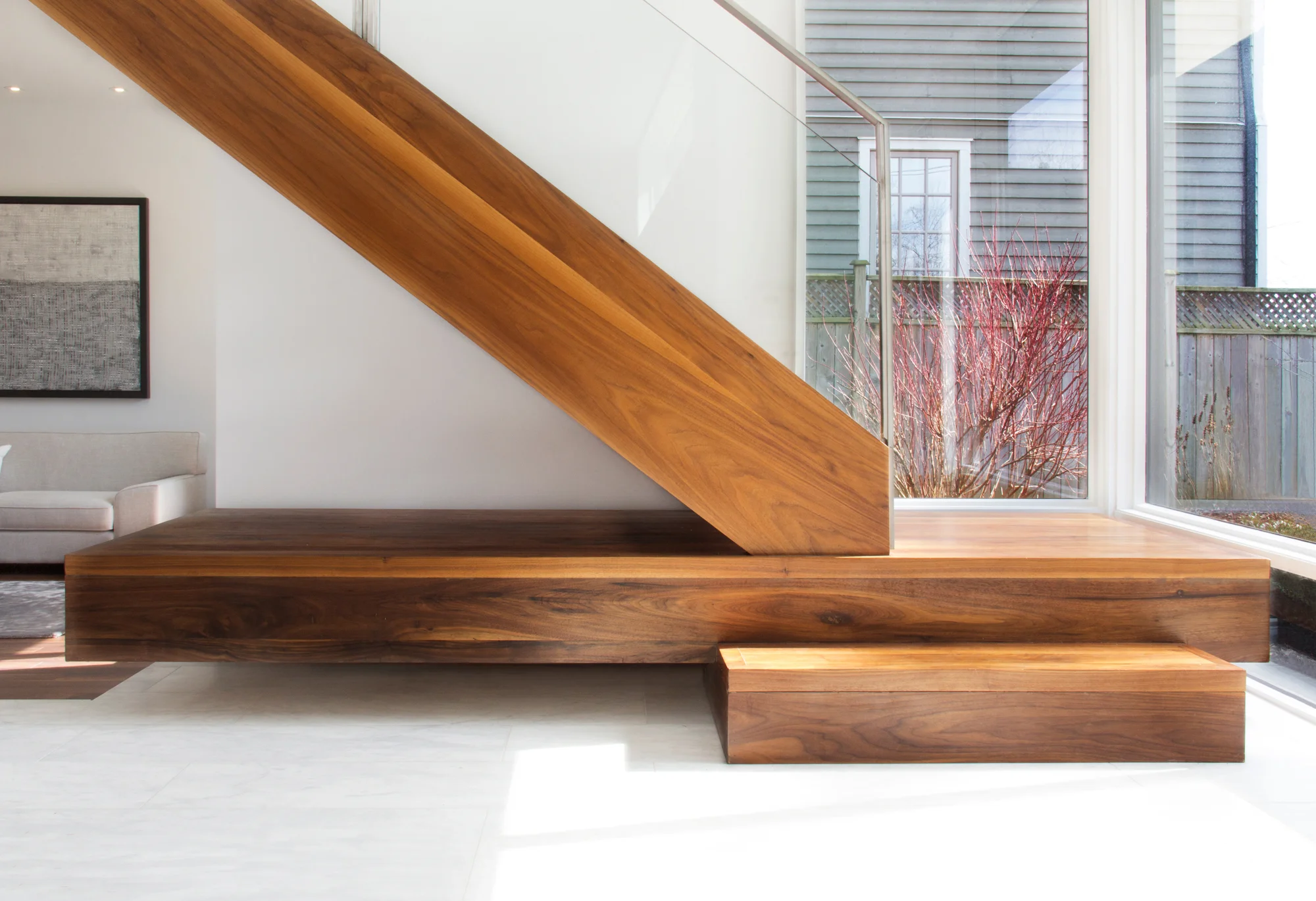 The focus of the two-storey foyer is an open tread walnut staircase with a stainless steel and glass guard. The main staircase is perched on a cantilevered platform which is used as a bench for seating at the front entrance.