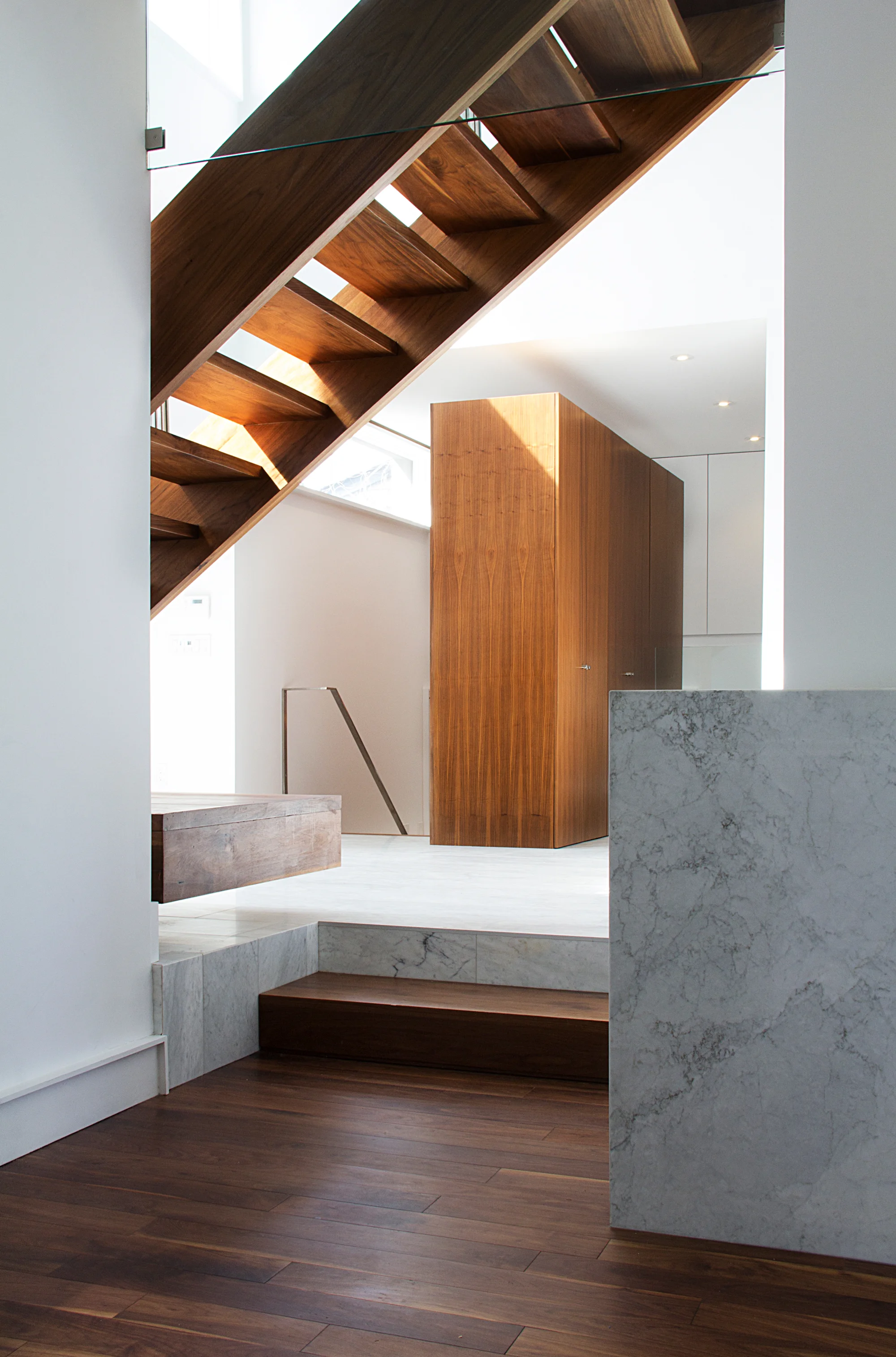 The U-shaped basement staircase winds around a walnut “block” which houses coats and shoes accessed from three floor levels. Two coat closets are accessed from the first floor, a large shoe closet from the mezzanine garage level and an additional shoe and coat closet from the basement level.
