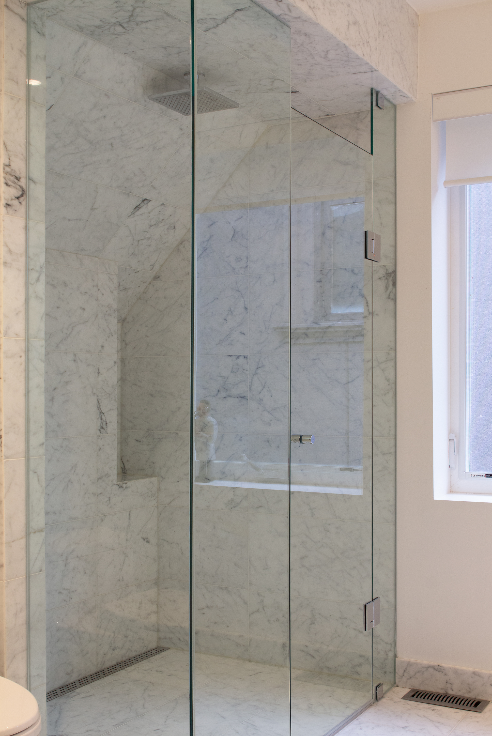 The frameless glass corner visually expands the marble-clad shower.