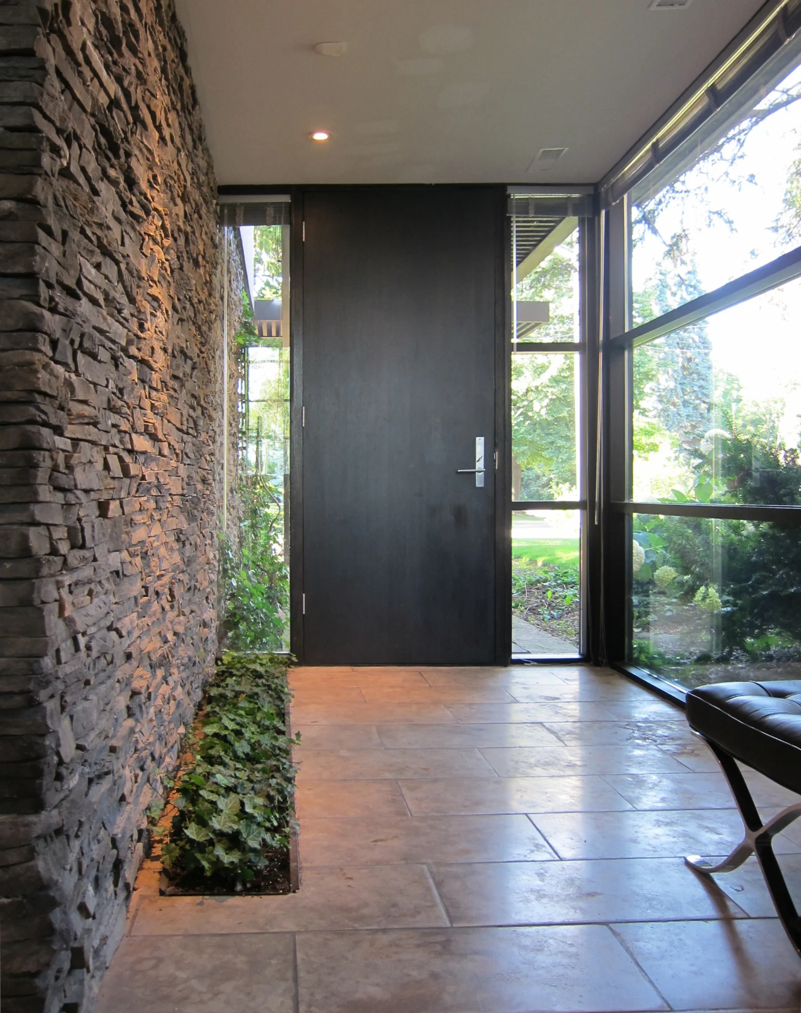 The foyer addition was constructed at grade level internalizing the stairs to the main floor. Lowering the front door and foyer windows to grade level permits the integration of the interior and exterior, grounding the house. A stone wall and ivy planting area continues through the slot window emphasizing the interior and exterior connection.