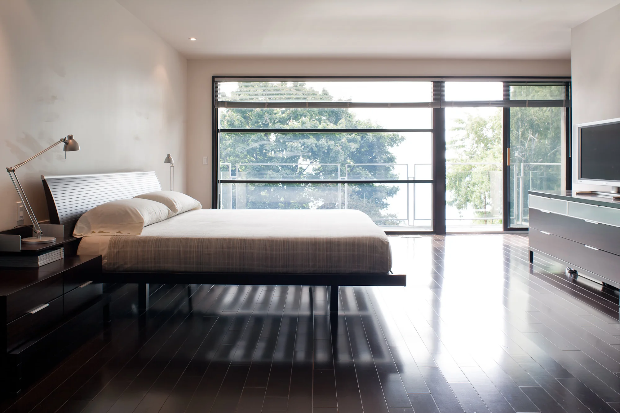 The master bedroom features floor-to-ceiling windows which overlook Lake Ontario. A balcony is accessible through the patio door. The balcony’s glass balustrade allows unrestricted views from the interior.