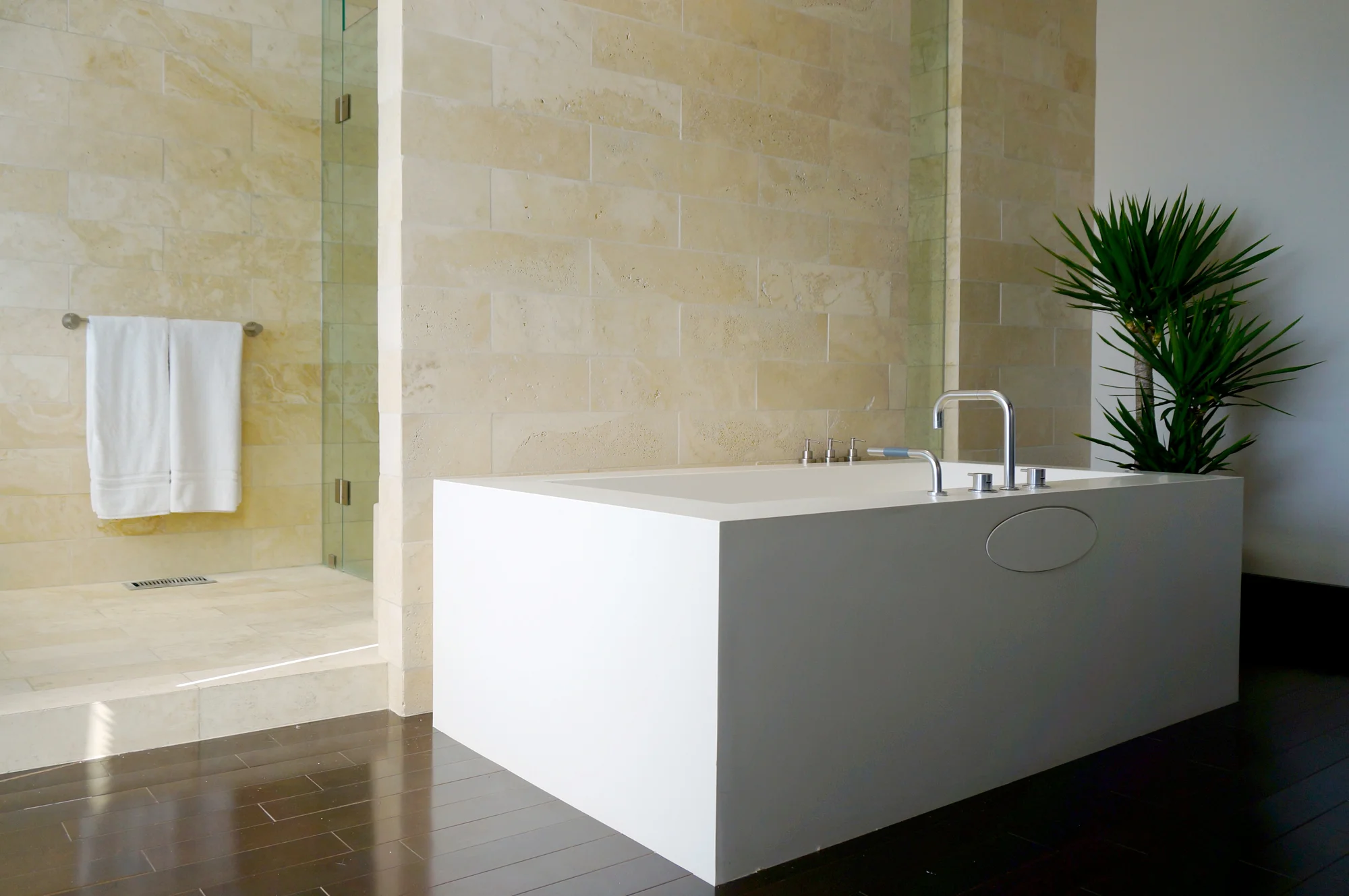 A limestone wall separates the WETSTYLE bathtub and the large glass fronted shower enclosure which offers a lake view.