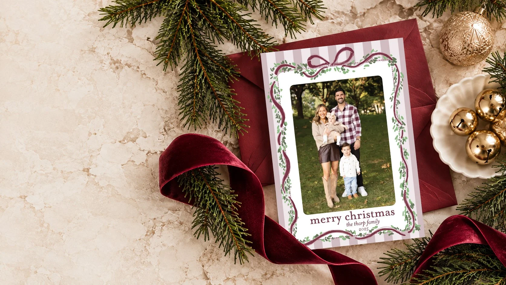 Custom family Christmas card with burgundy ribbon and festive greenery, designed by Studio Kate