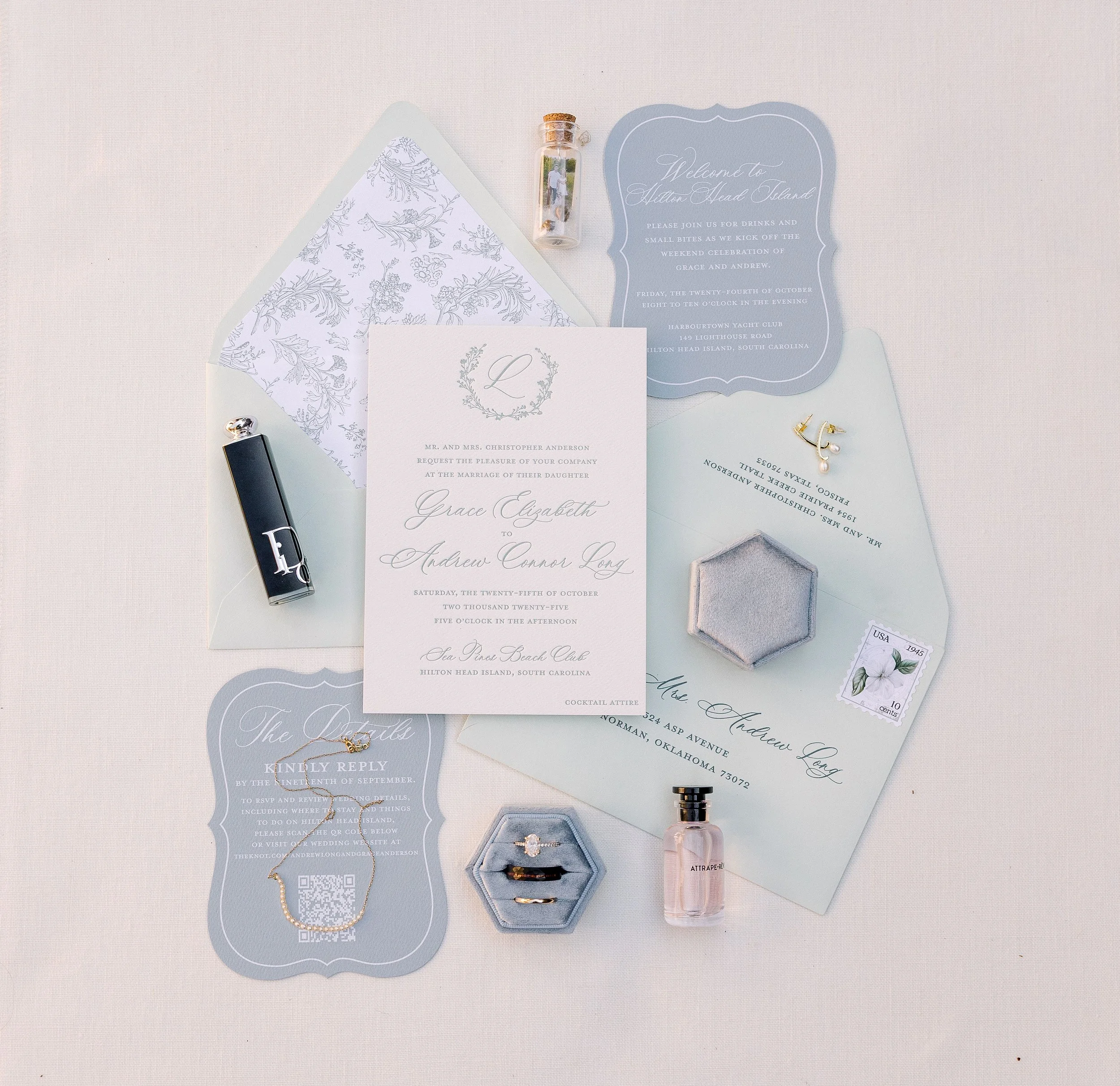 Wedding invitation suite with floral patterns, RSVP card, jewelry, perfume, and small decorative objects on a light background.