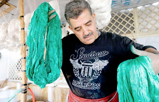 Mohammad Al Rihawi dips silk threads into green dye on January 23, at his atelier in the Syrian capital Damascus (AFP photo)