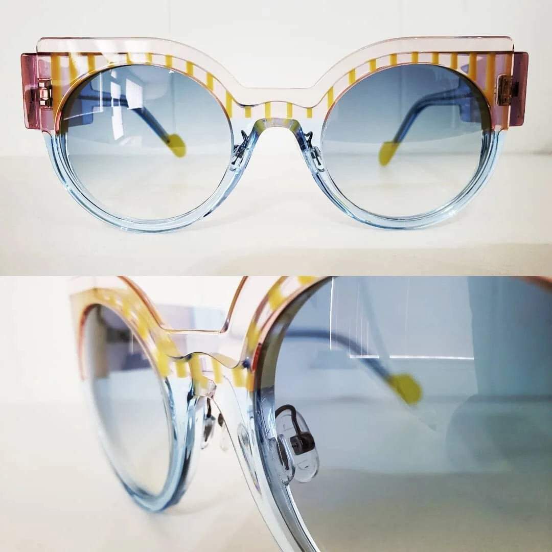 Colorful sunglasses with round blue lenses and yellow and pink striped frames placed on a white surface.
