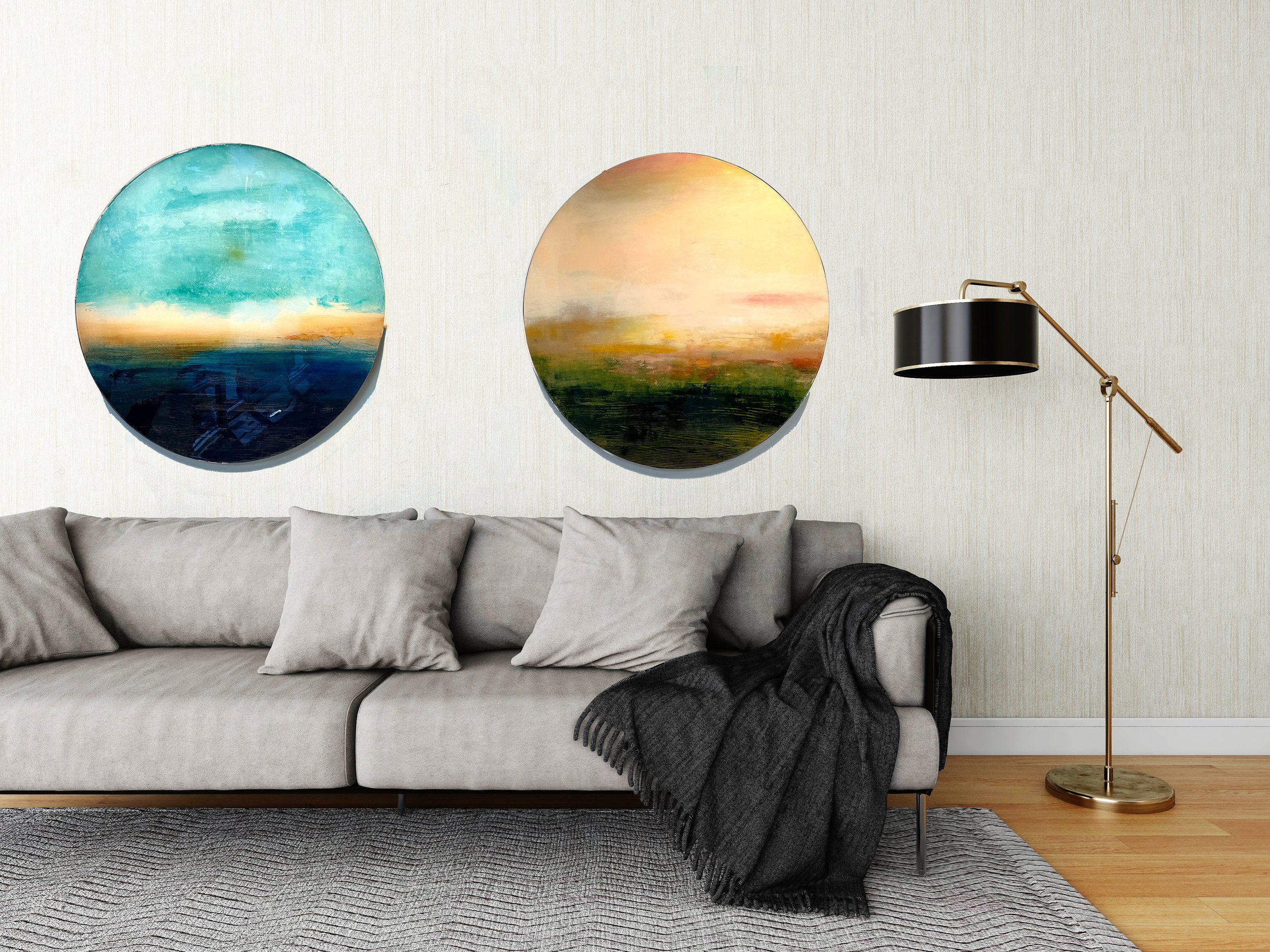 Living room with a light gray sofa, four matching pillows, a gray throw blanket, two round landscape paintings on the wall, a black and gold floor lamp, a gray textured rug, and wood flooring.