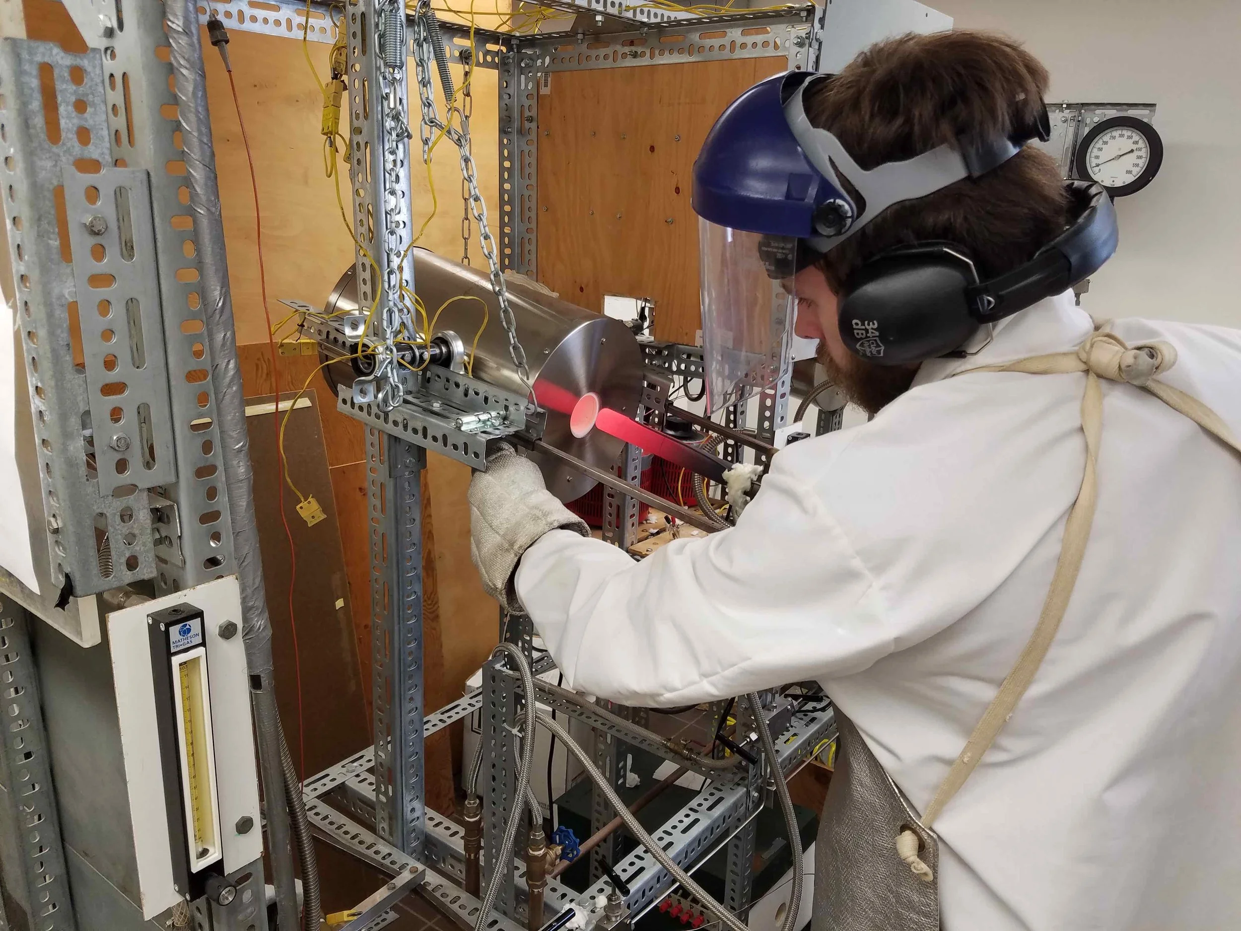 Image is of Austin Gion removing a MHC (Molybdenum-Hafnium-Carbide) cold-seal pressure vessel from a furnace at the completion of an experiment.