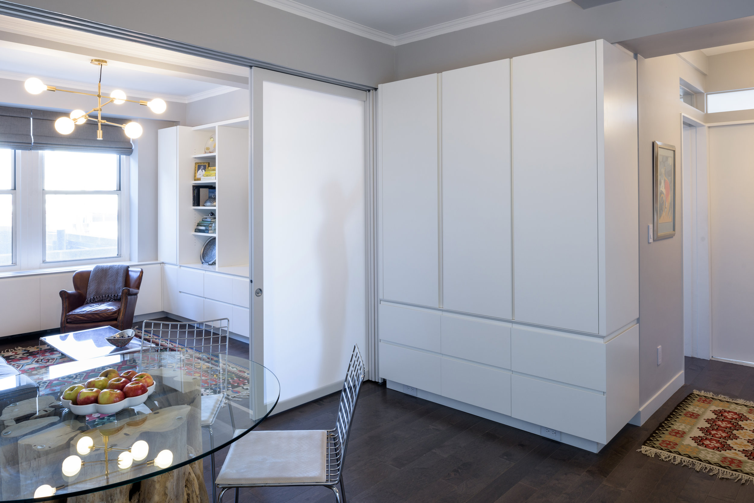 Next, the closet dividing the kitchen from the foyer and other spaces of the co-op was eliminated to increase the size of the kitchen and link it back to the rest of the apartment. With a more open layout, Fundamental introduced millwork to add more storage and to visually tie all of the living and entertaining spaces together. The bedroom at the back of the apartment was retained as the new master bedroom and the front of the apartment was opened up to create a more gracious living and dining space that takes advantage of the northern and southern windows.